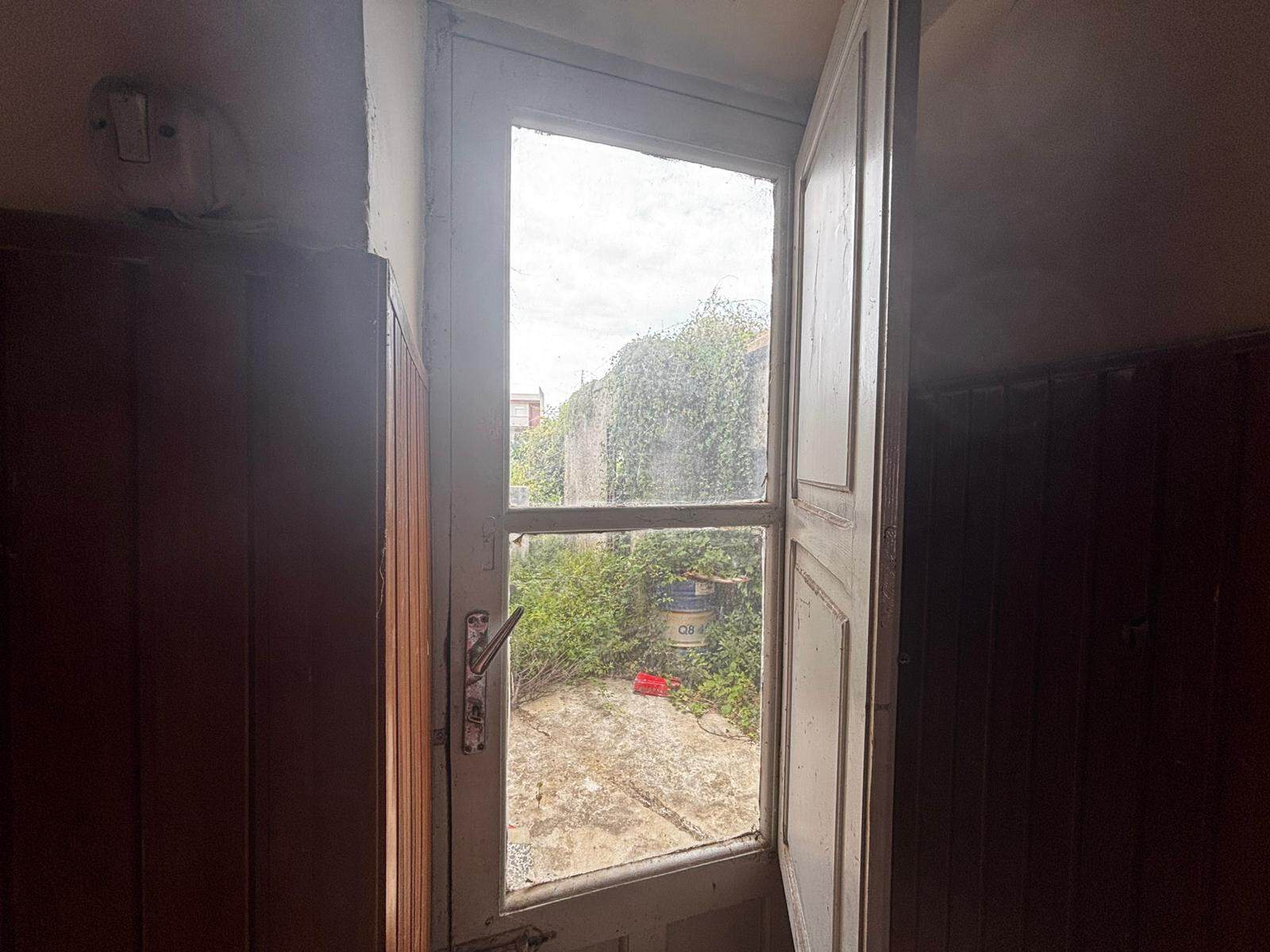 Vetrata di una finestra in legno con vista su un giardino e un cielo nuvoloso, all'interno di una stanza con pareti in legno scuro.