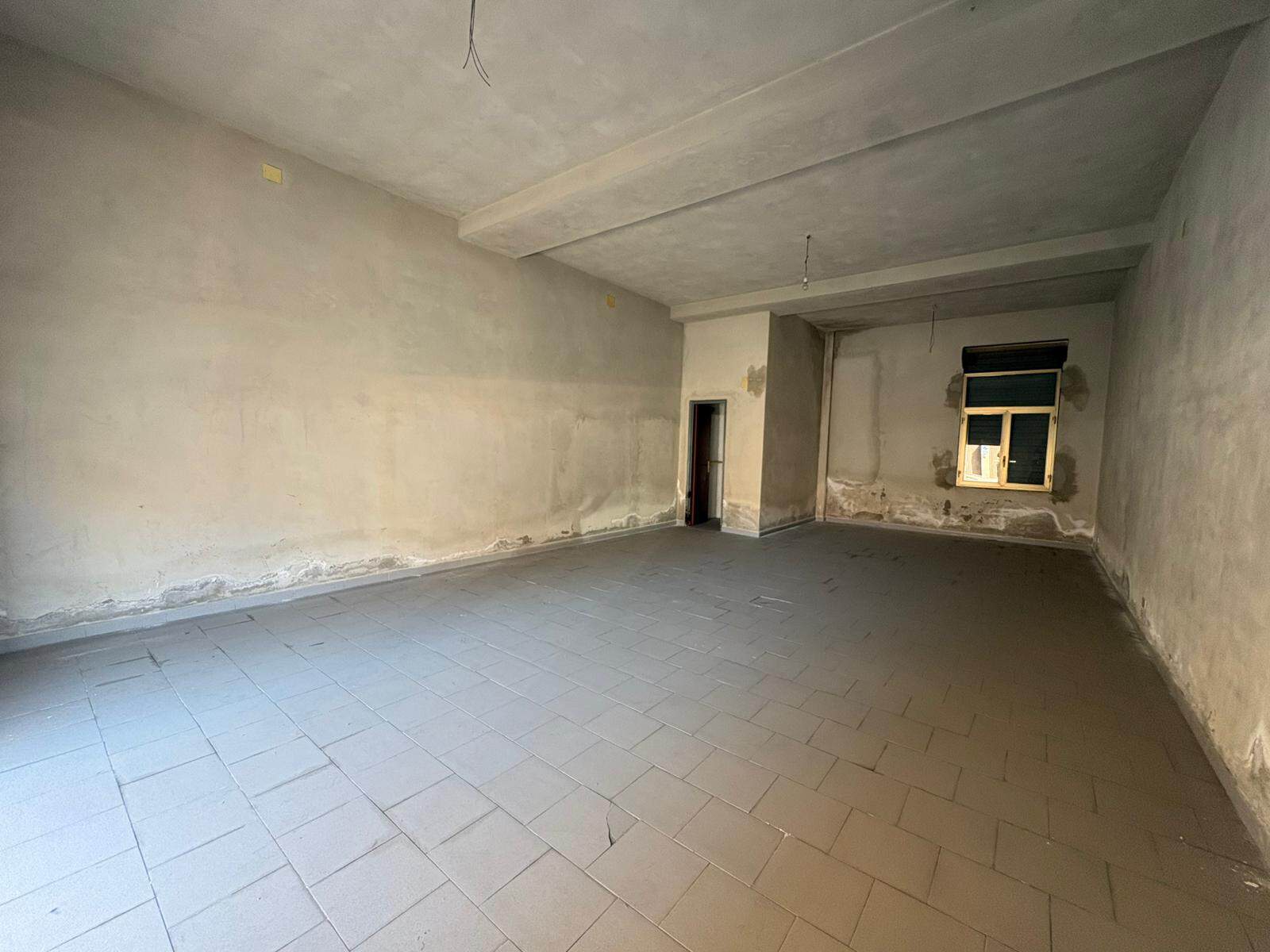 Interno di un appartamento in fase di ristrutturazione con pareti e soffitto in cemento grezzo e pavimento in piastrelle.