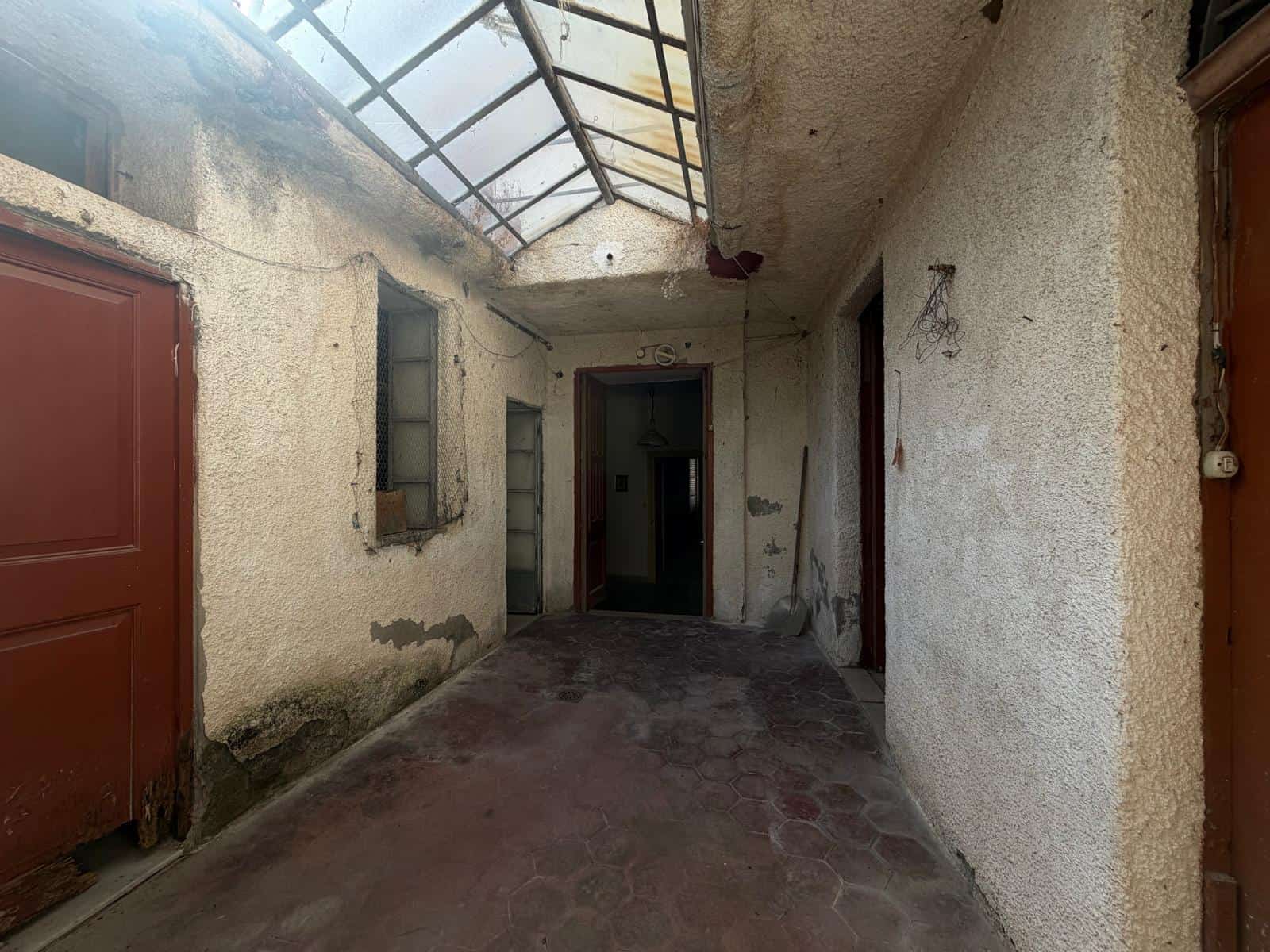 Ingresso di una casa indipendente con soffitto in vetro e pareti in pietra, in condizioni di abbandono.