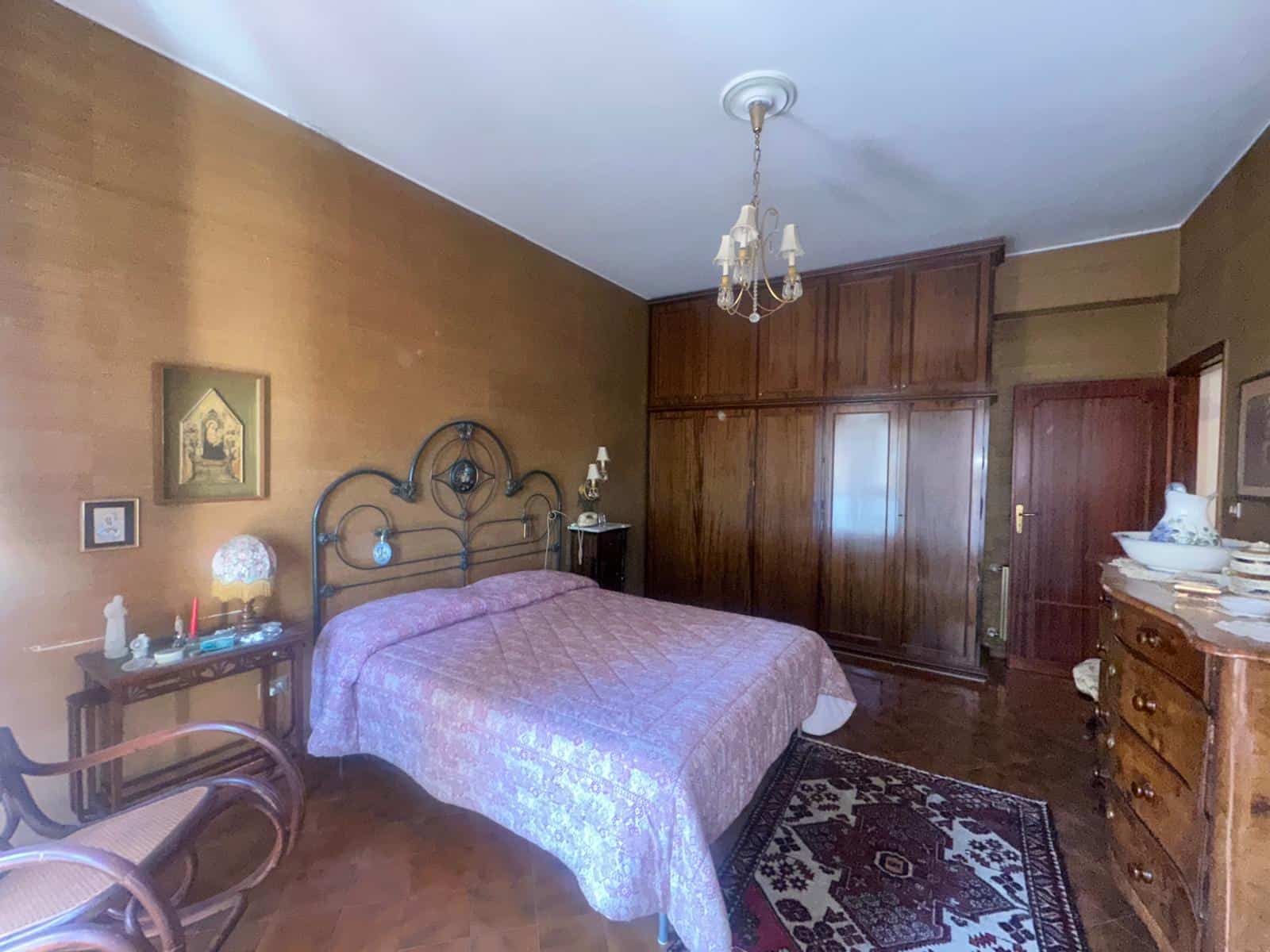 Il letto matrimoniale in una camera da letto classica con mobili in legno, pareti colorate e un tappeto decorativo, ideale per case in stile tradizionale o rustico.
