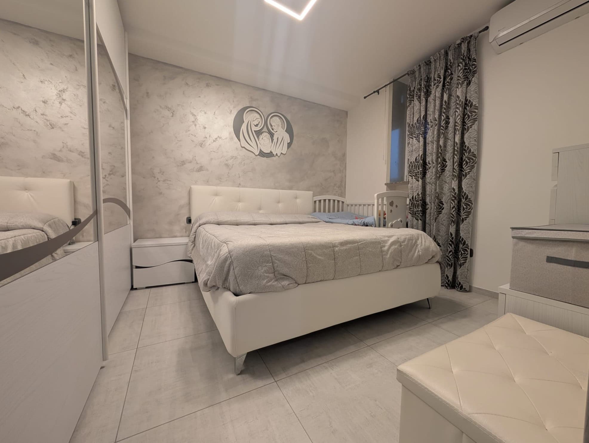 Camera da letto moderna con parete decorativa in stile marmo, letto bianco, armadio a specchio e tende nere e bianche, ambiente luminoso e elegante.