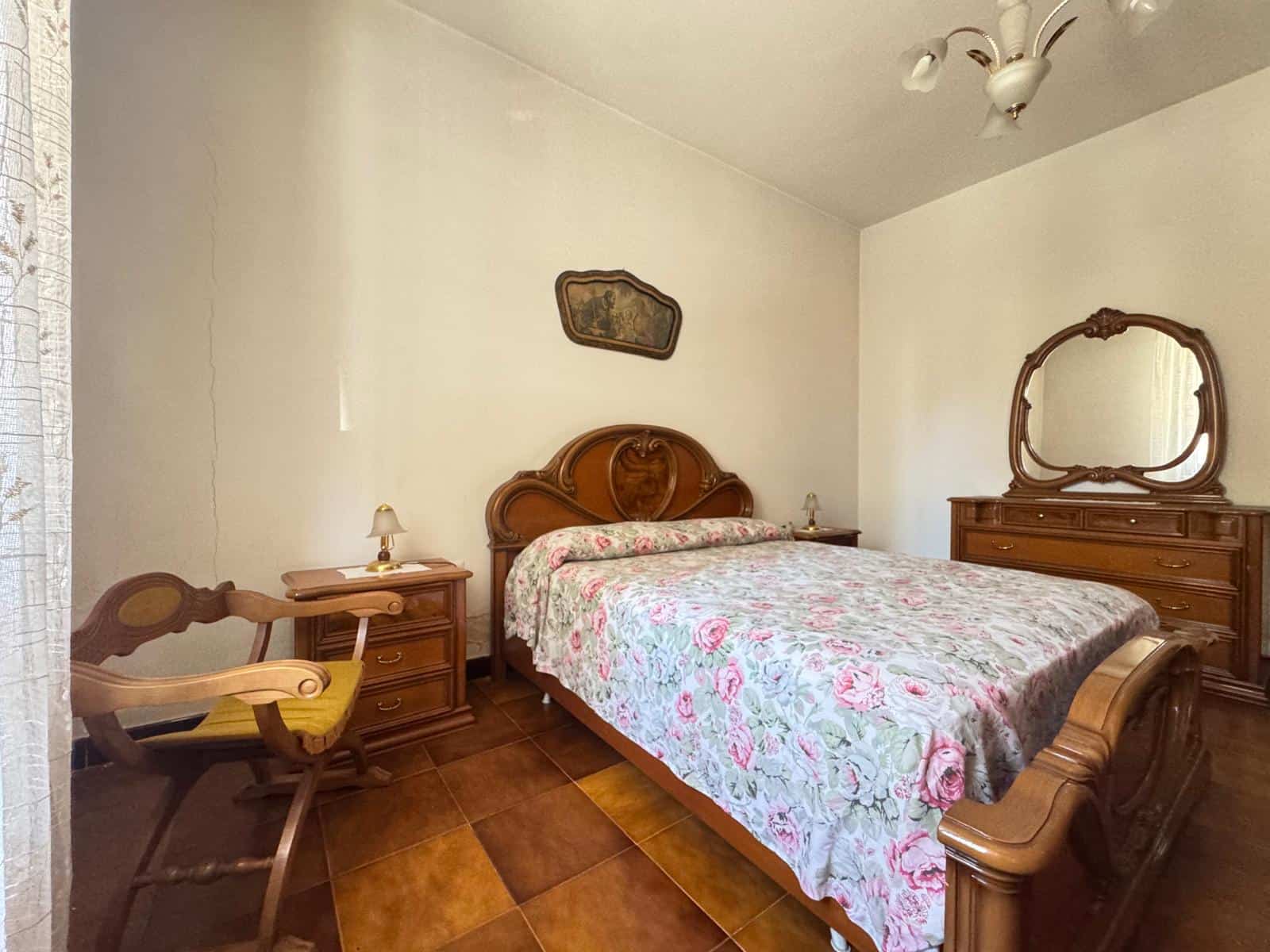 Il letto matrimoniale in stile classico con testiera in legno, in una camera da letto accogliente e ben arredata, con mobili in legno e decorazioni vintage, ideale per ambienti di charme.
