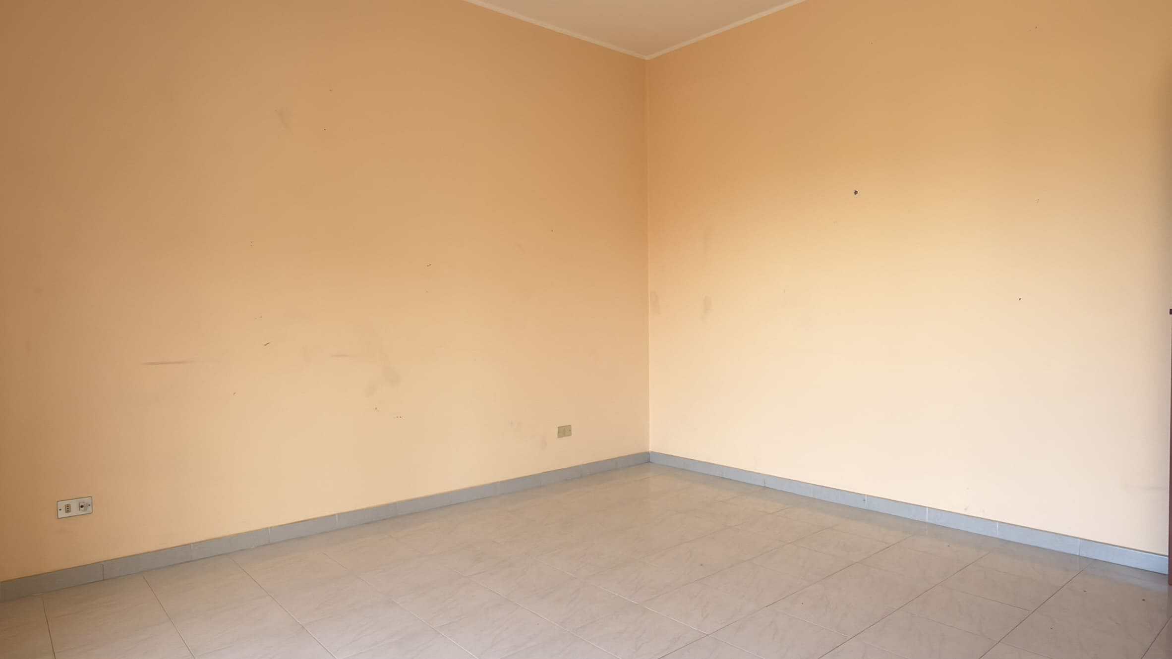 Stanza vuota con pareti beige e pavimento in piastrelle chiare, ideale per arredamento e ristrutturazione.