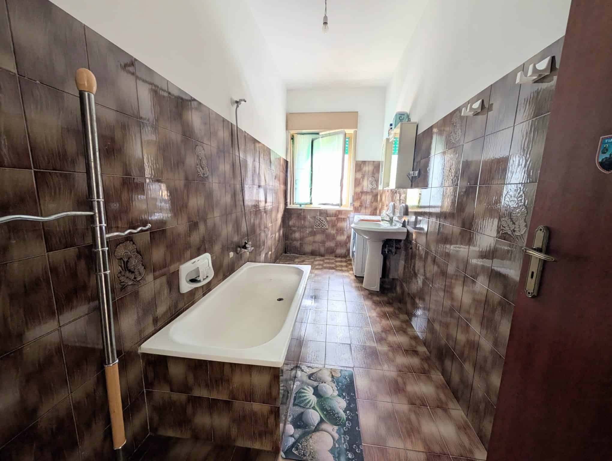 Bagno spazioso con vasca, lavabo e finestra, arredato in stile semplice e funzionale.