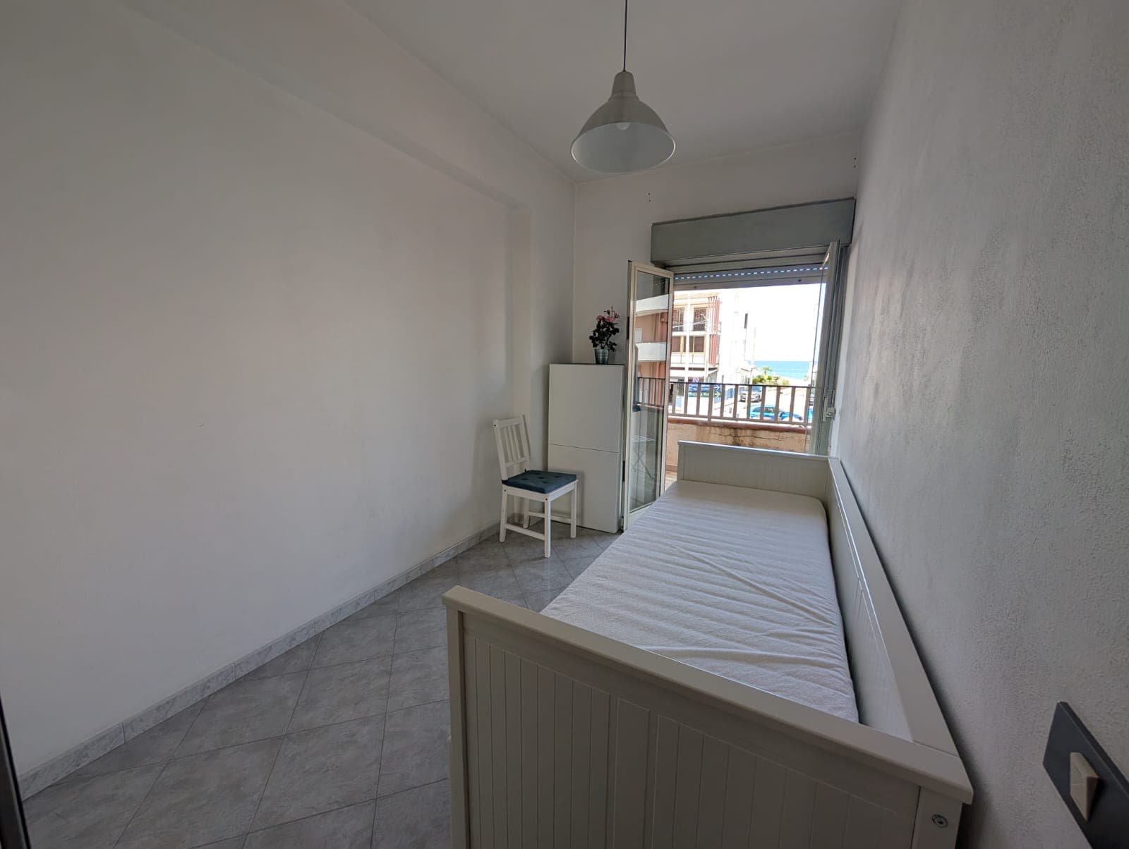 Soggiorno luminoso con letto singolo, finestra con vista su balcone e arredamento minimalista, ideale per affitti brevi o studenti, in zona tranquilla e ben servita.