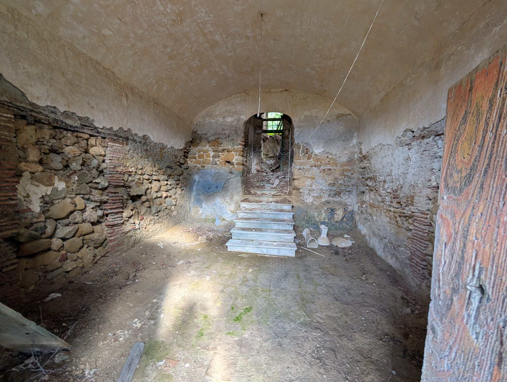 Interno di un rudere con pareti in pietra e mattoni, ingresso con scala in pietra, ambiente rustico e abbandonato.
