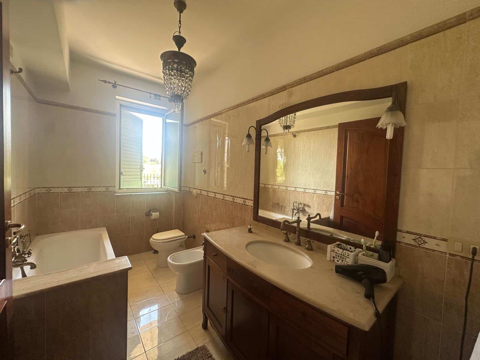 Bagno spazioso con lavabo in legno, grande specchio e vasca, illuminato da luce naturale e lampada a soffitto.