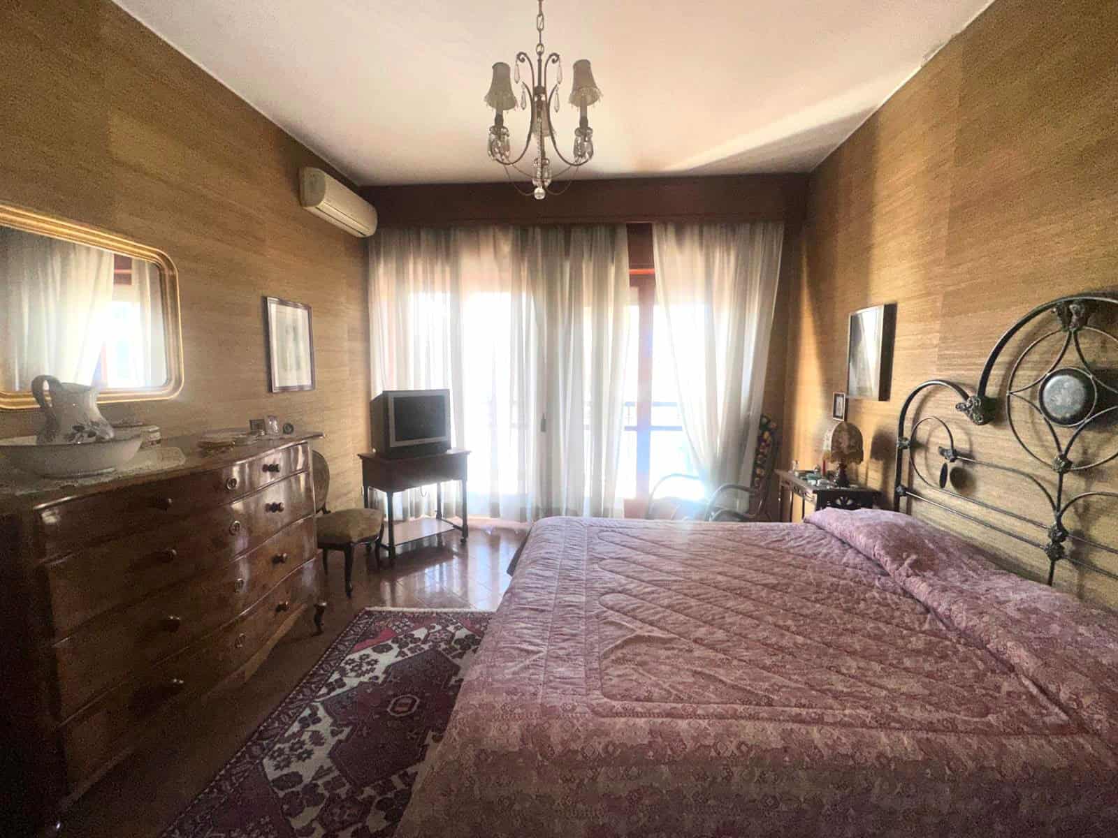 Camera da letto spaziosa con arredi classici, letto grande, tende luminose e decorazioni eleganti, ideale per un soggiorno confortevole e accogliente.