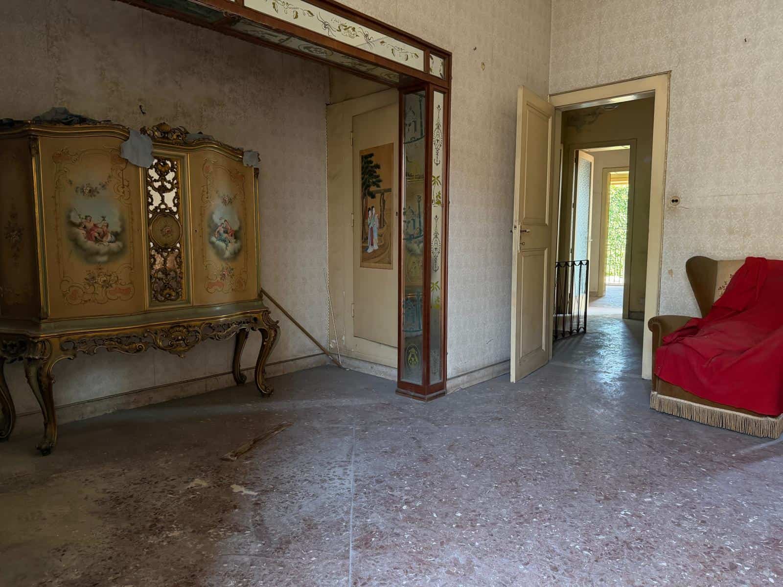 Interno di una casa indipendente con arredi d'epoca e pareti decorate, ingresso e soggiorno con porta aperta verso un balcone.
