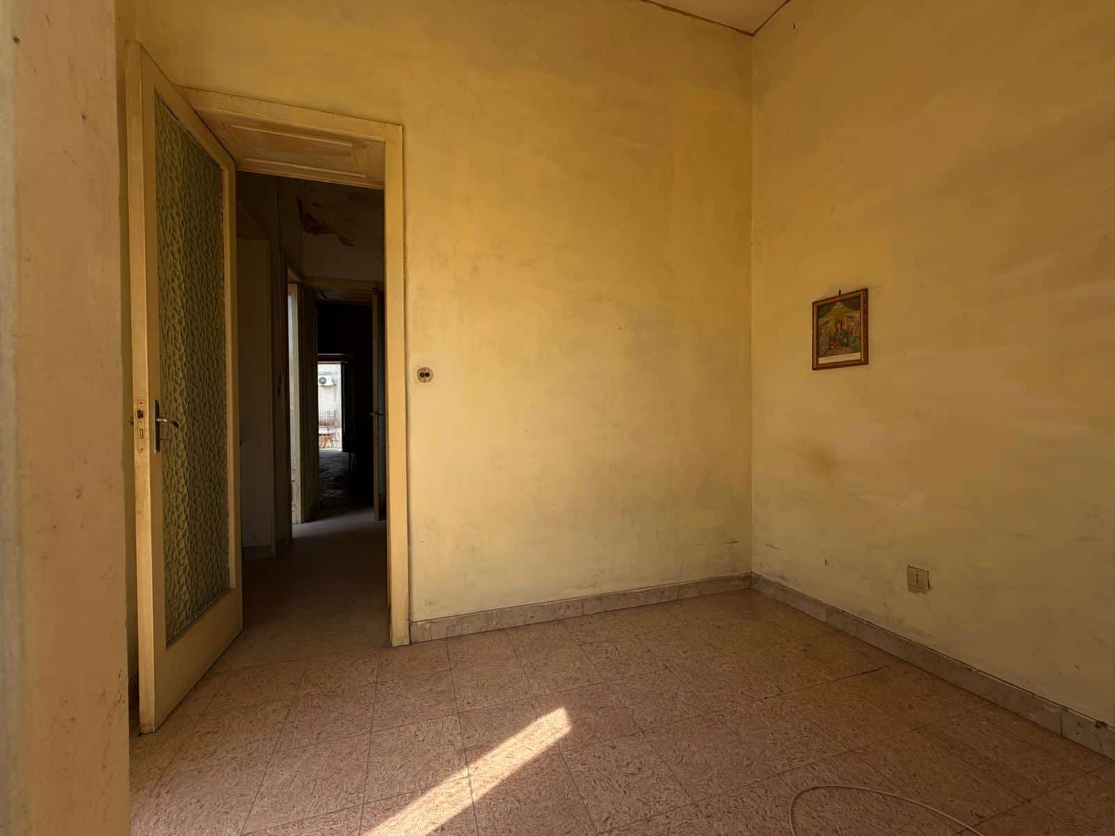 Stanza vuota in un appartamento in vendita a Barcellona P.G., con pareti gialle e pavimento in piastrelle, luce naturale che entra dalla finestra.