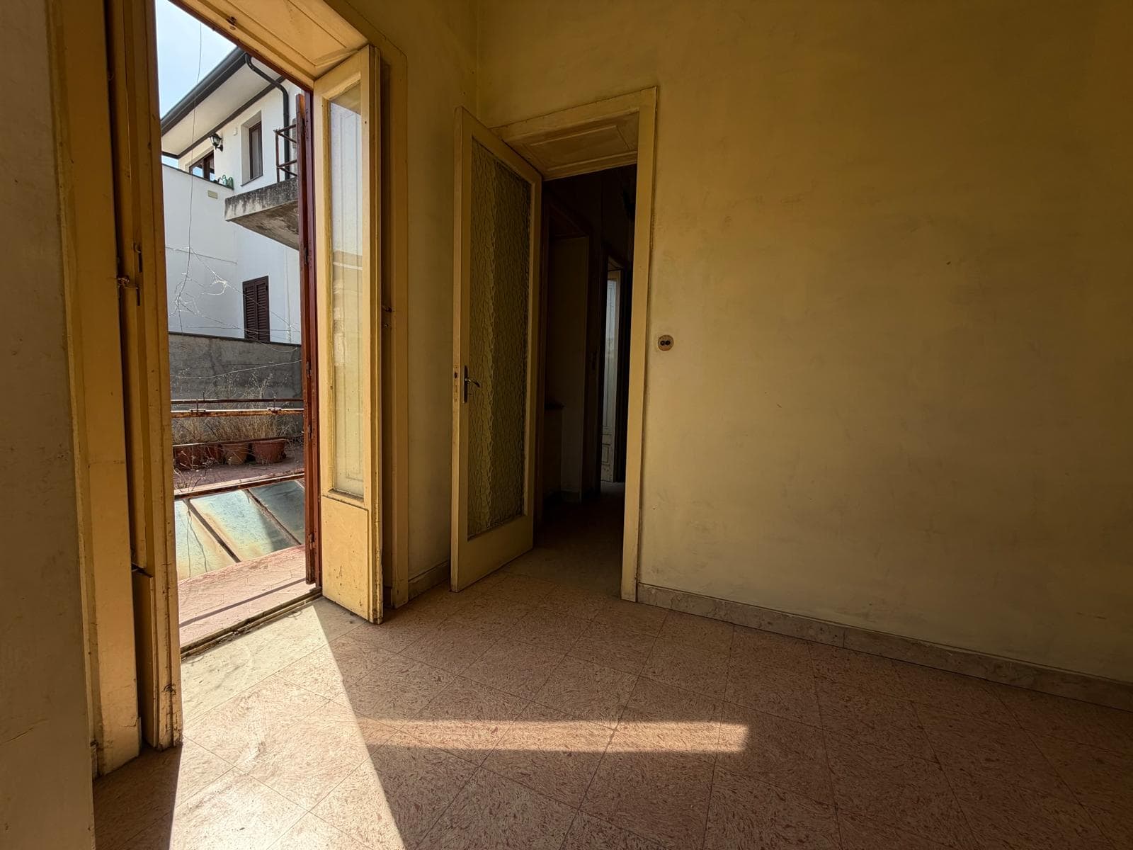 Vista di una stanza vuota con porta finestra che dà su un balcone, luce naturale entra nell'ambiente.