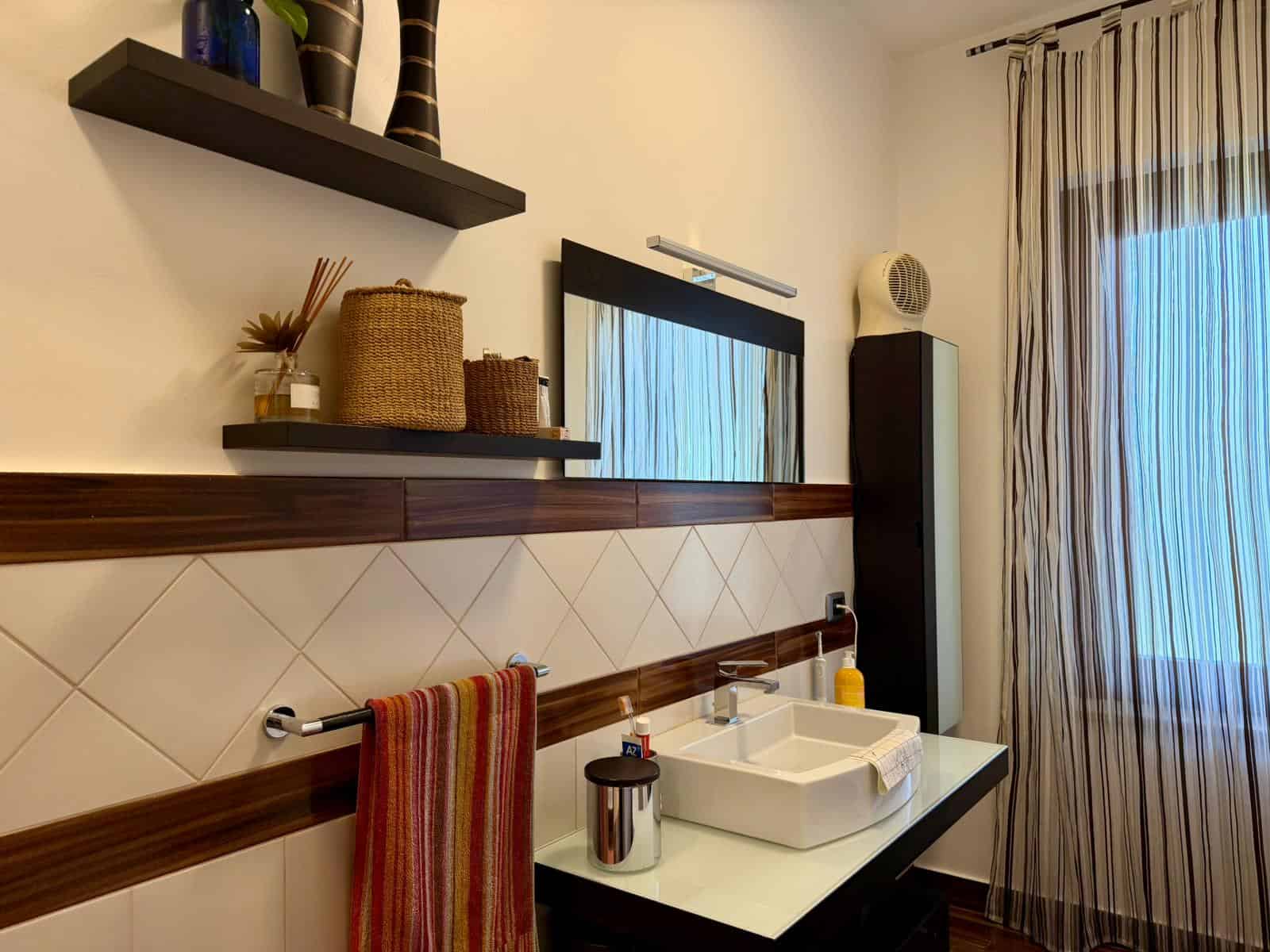 Bagno moderno con lavabo a incasso, specchio e tende a righe in un'abitazione in Sicilia.