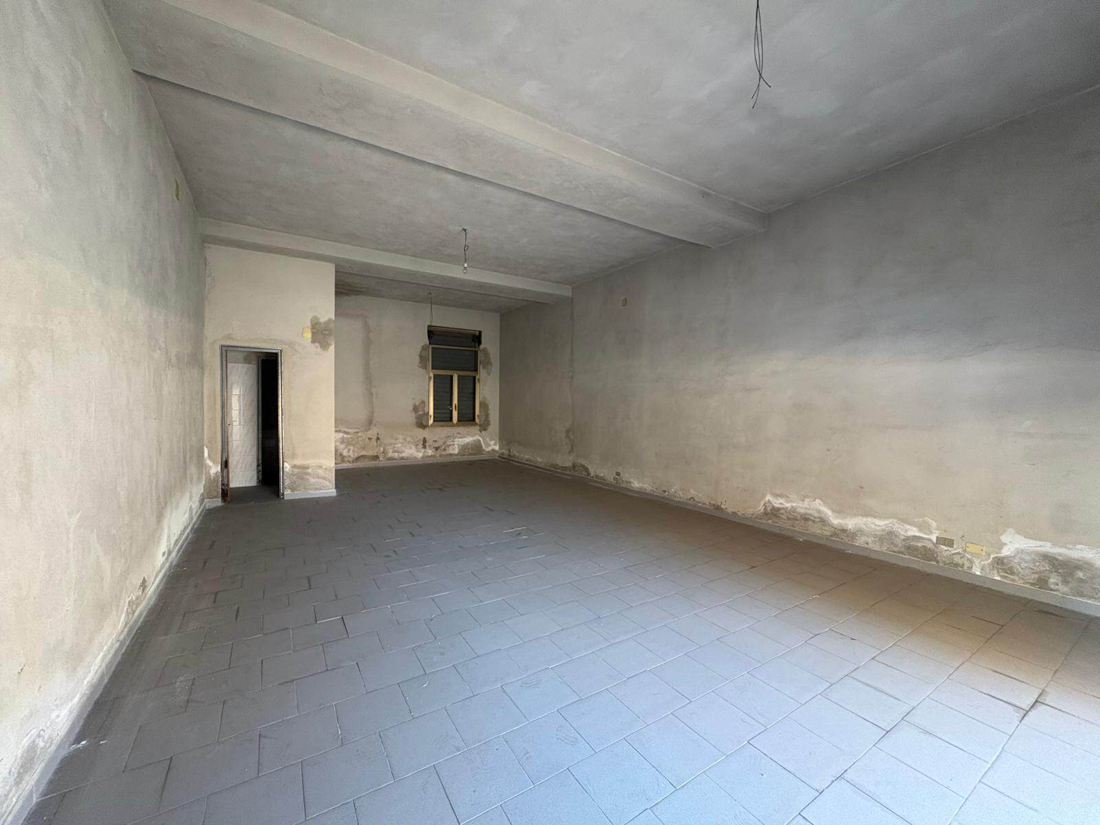 Interno di un appartamento in fase di ristrutturazione con pareti grezze e pavimento in piastrelle.
