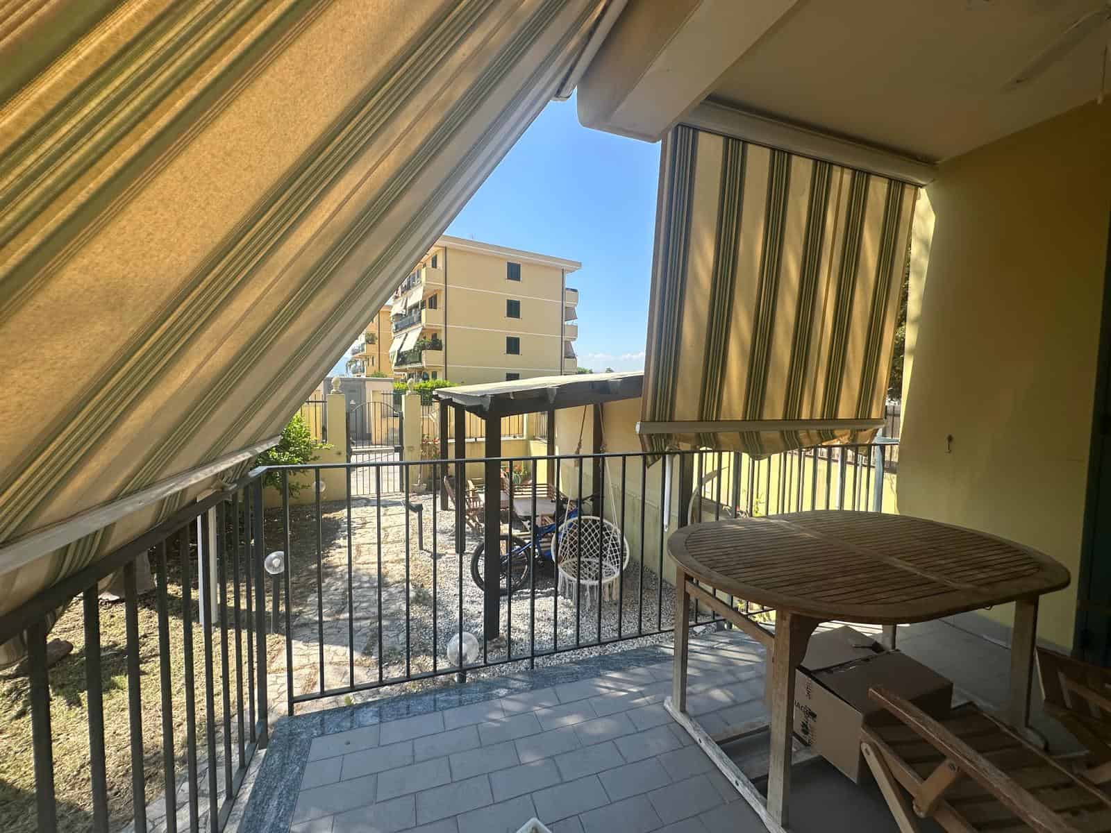 Balcone di un appartamento con tende a strisce e vista su edifici residenziali a Milazzo, Sicilia.