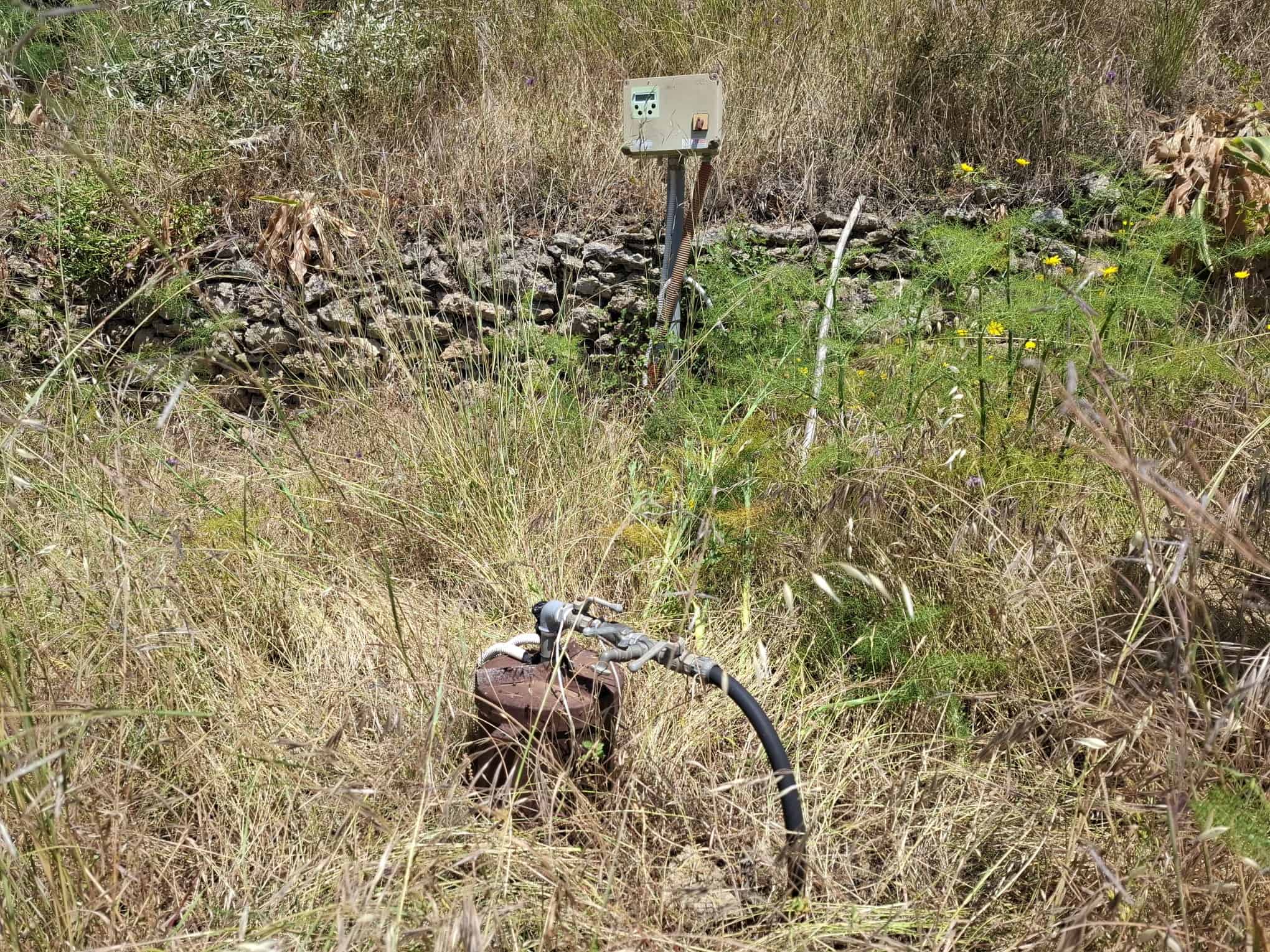 Sistema di irrigazione automatico in un campo naturale con erba secca e vegetazione selvaggia, pronto per l'uso agricolo o orticolo.