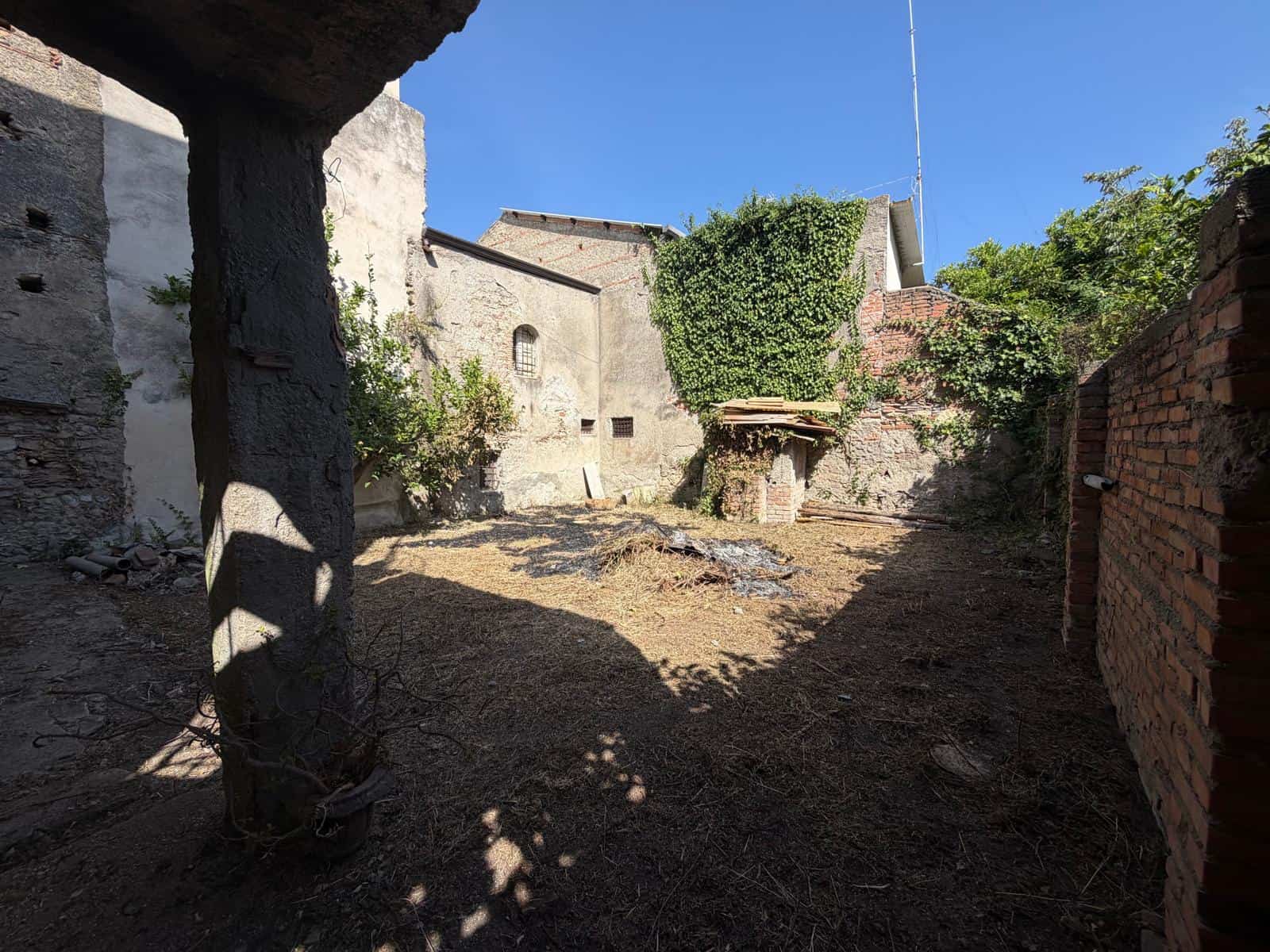 Cortile interno di una casa indipendente in vendita a Barcellona P.G., con pareti in pietra e mattoni, e un albero che fornisce ombra.
