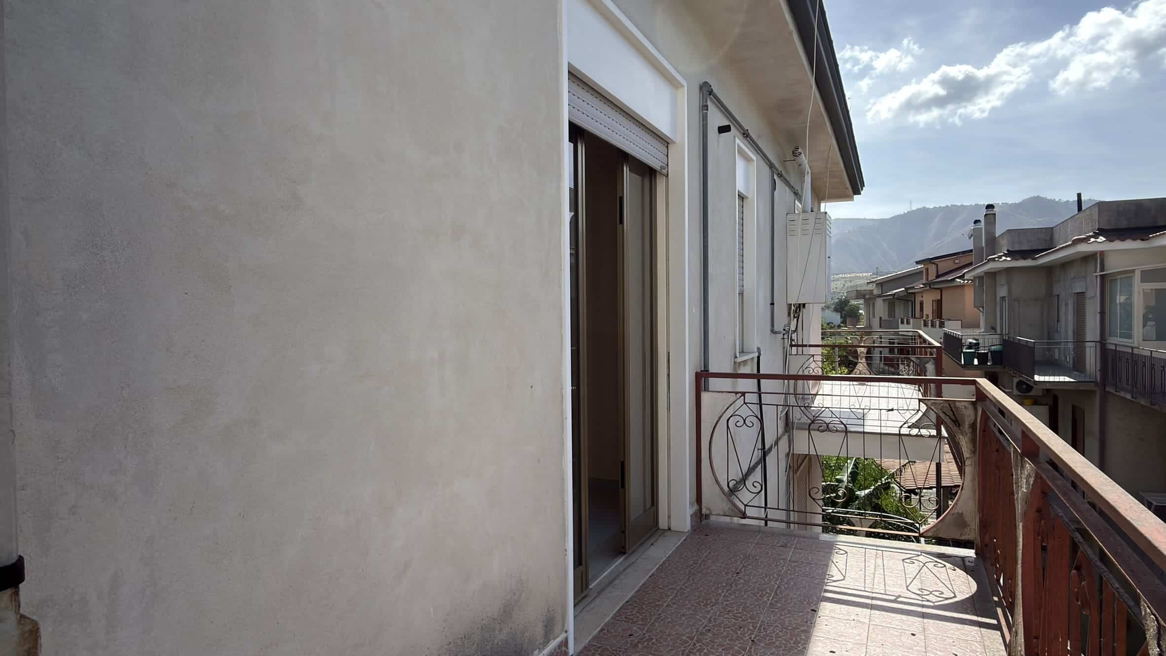 Balcone di un appartamento con vista sulle case e sulle montagne in lontananza, in un giorno soleggiato.