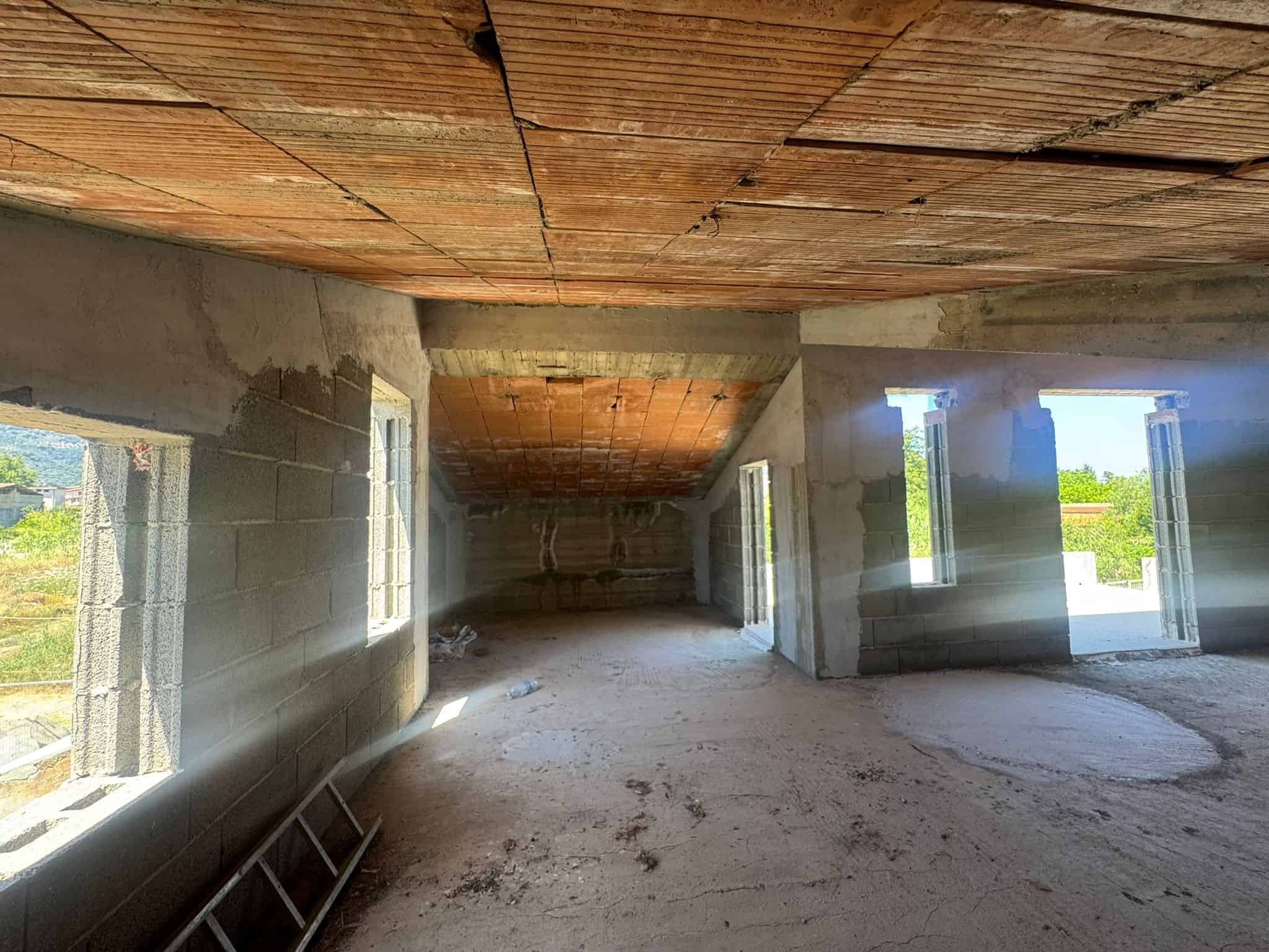 Interno di un edificio in costruzione con pareti in cemento e soffitto in mattoni, luce naturale che entra dalle finestre aperte.