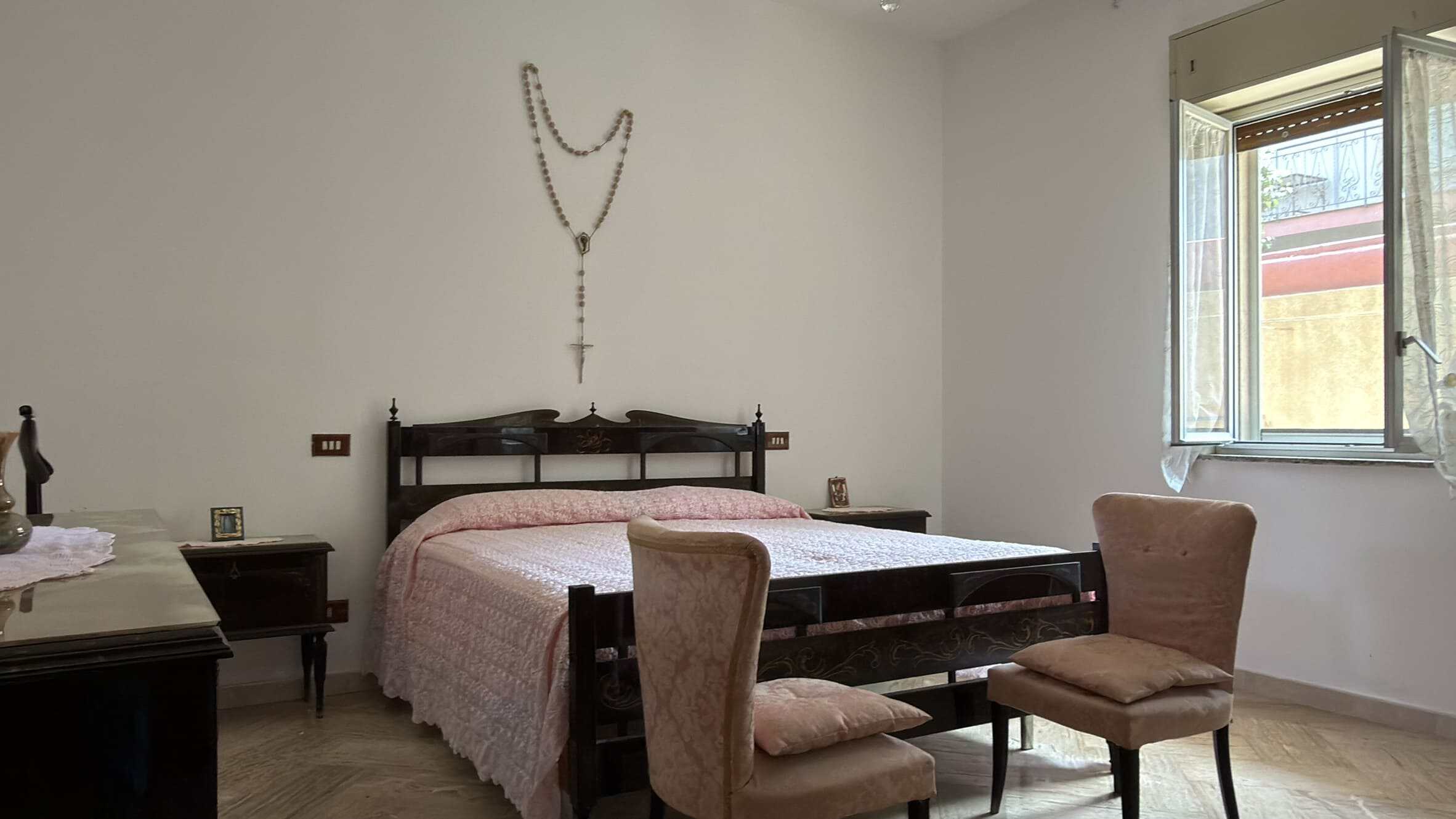 Camera da letto spaziosa con letto in legno, due sedie e finestra che lascia entrare luce naturale, ideale per case in vendita o affitto a NextCasa.