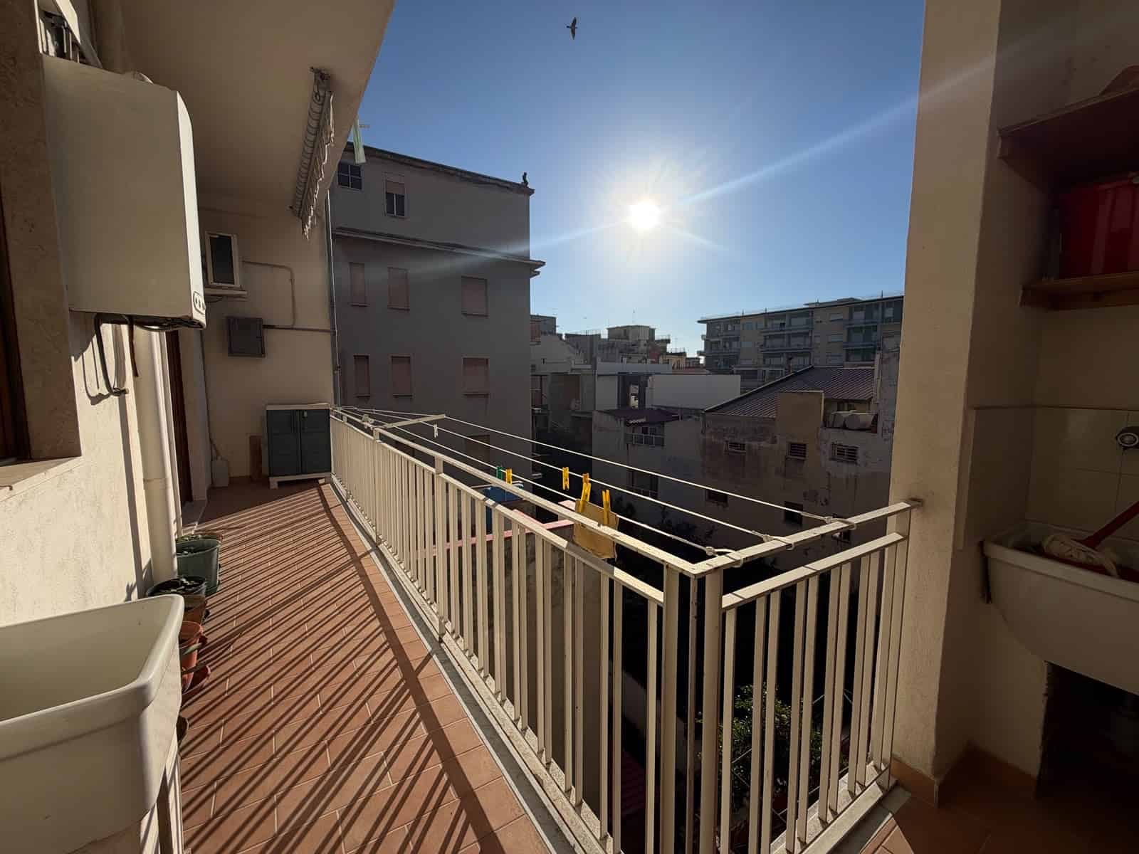 Balcone di un appartamento con vista sulla città e il sole splendente nel cielo.