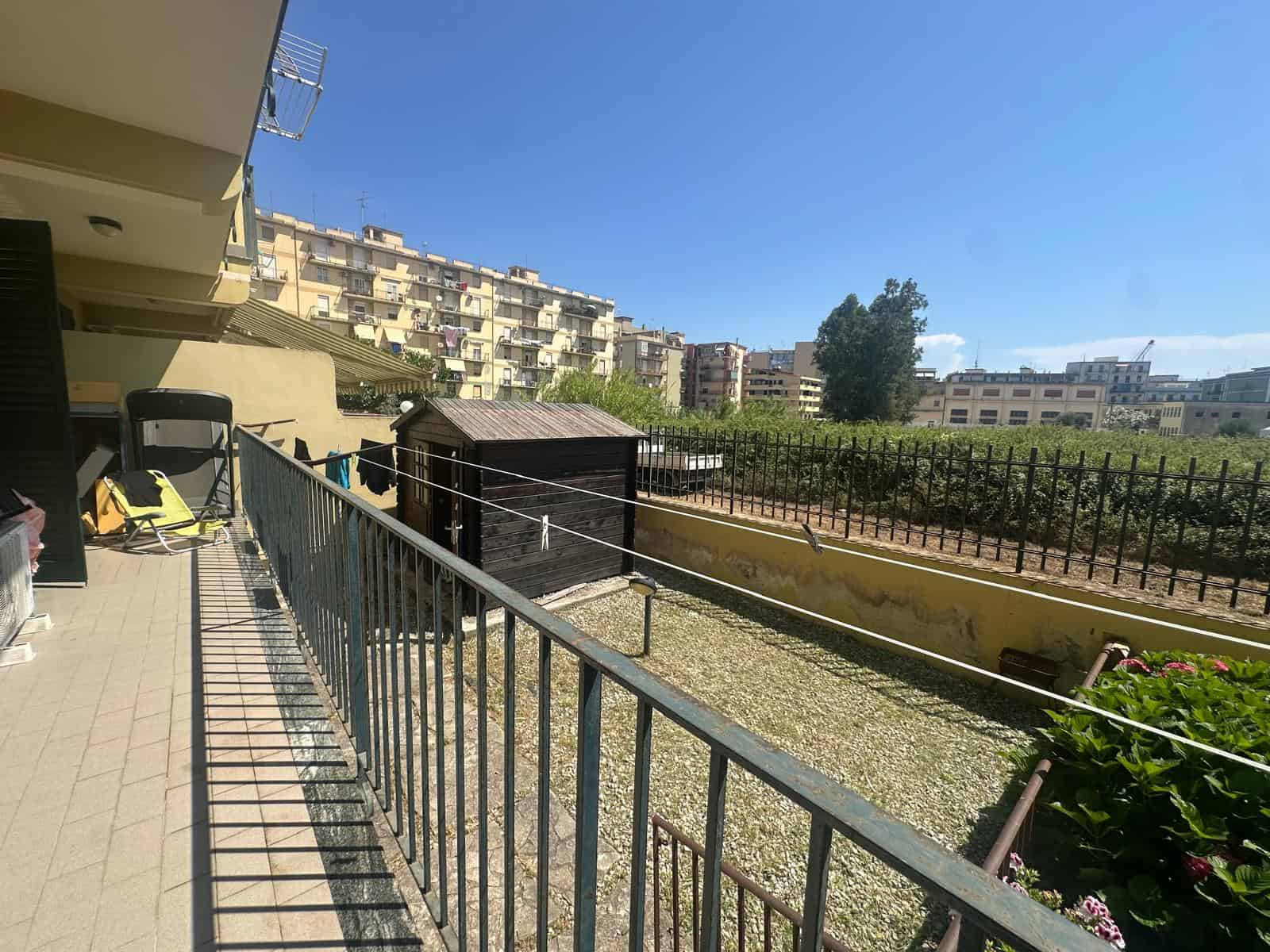 Balcone di un appartamento con vista su giardino e edifici residenziali a Milazzo, Sicilia.