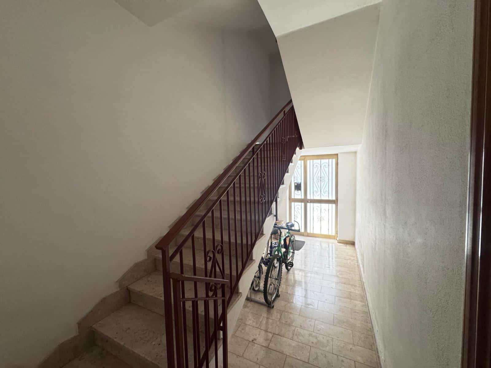 Scalinata interna di un edificio residenziale con ringhiera in metallo e biciclette parcheggiate, illuminata da luce naturale attraverso una finestra.