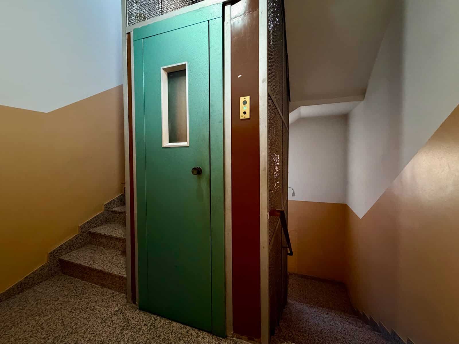 Ascensore condominiale in edificio con scale e pareti colorate, ambiente interno ben illuminato.