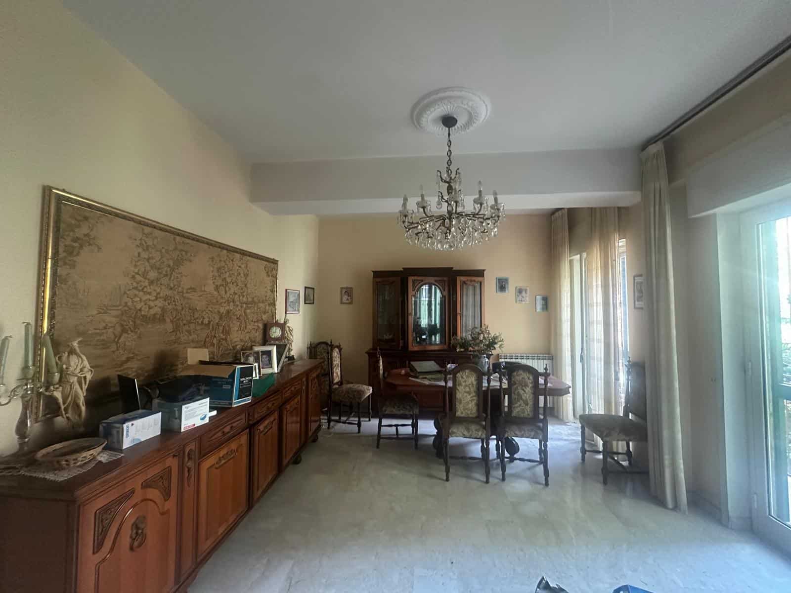Soggiorno elegante con mobili in legno, grande specchio e lampadario a cristalli, ambiente luminoso con accesso a balcone, ideale per vivere momenti di relax e convivialità.