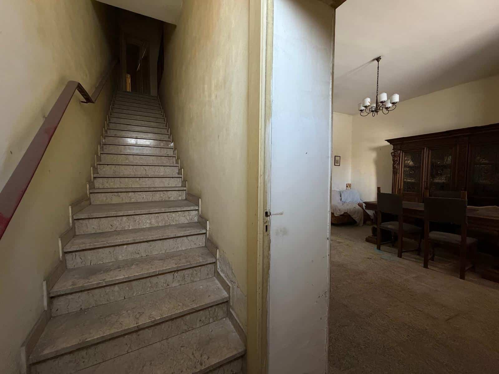 Interno di una casa con scala in marmo e zona pranzo con tavolo e sedie in legno.