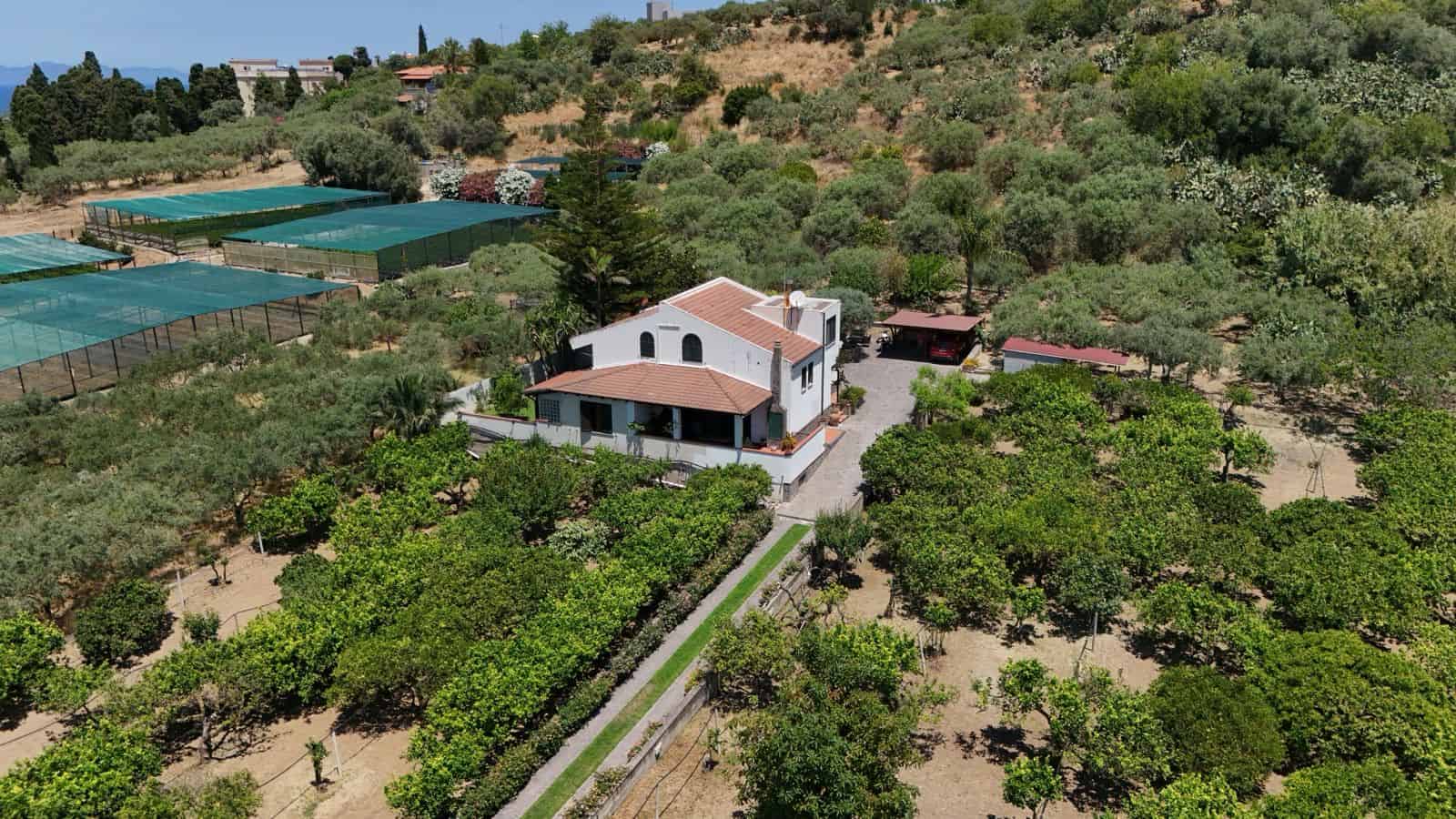 Villa singola in vendita a Terme Vigliatore, immersa in un ampio giardino con alberi e spazi verdi, vista panoramica sulla campagna siciliana.
