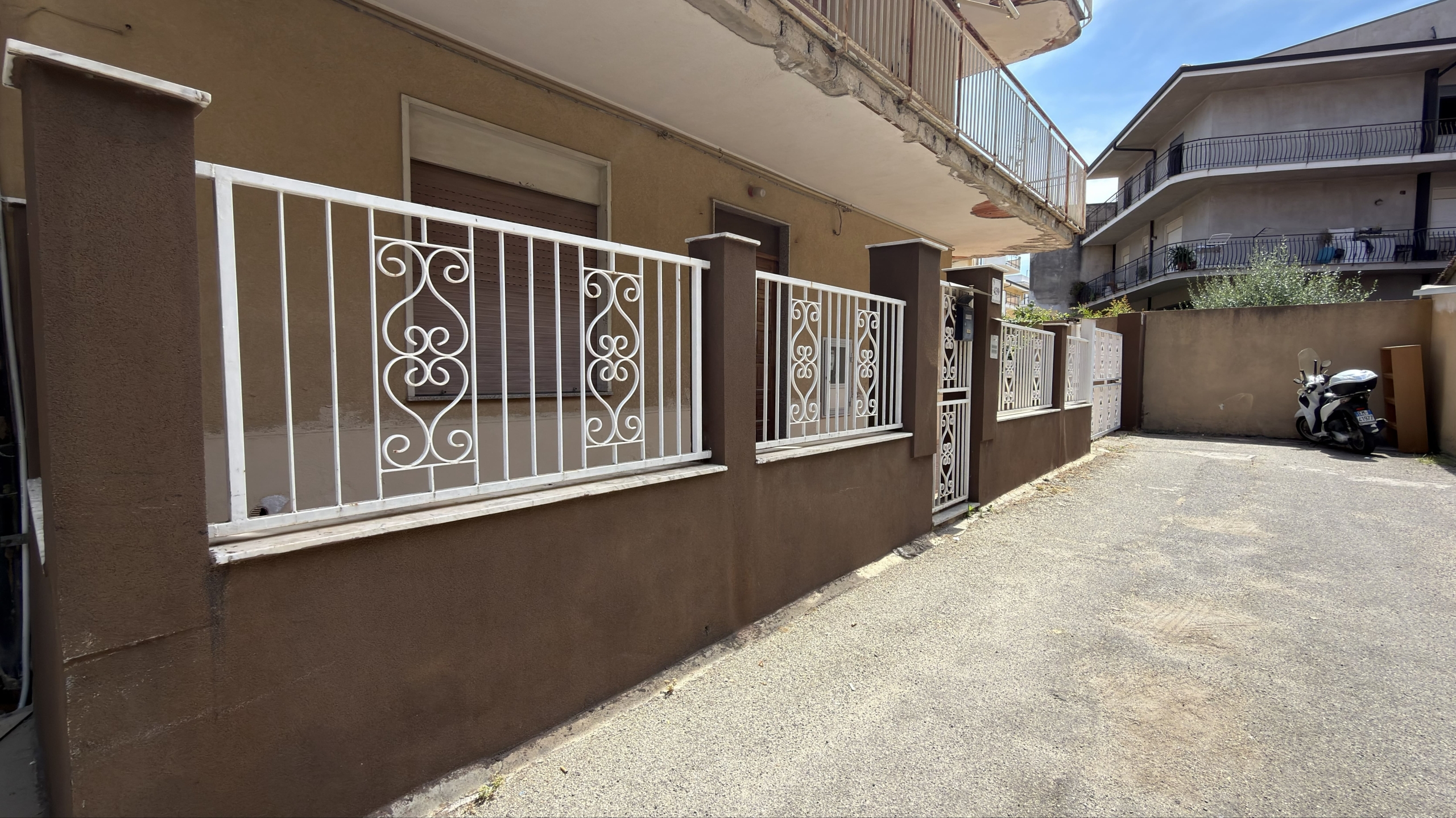 Balcone con ringhiera in ferro battuto bianco e pareti marroni, in un complesso residenziale a più piani.