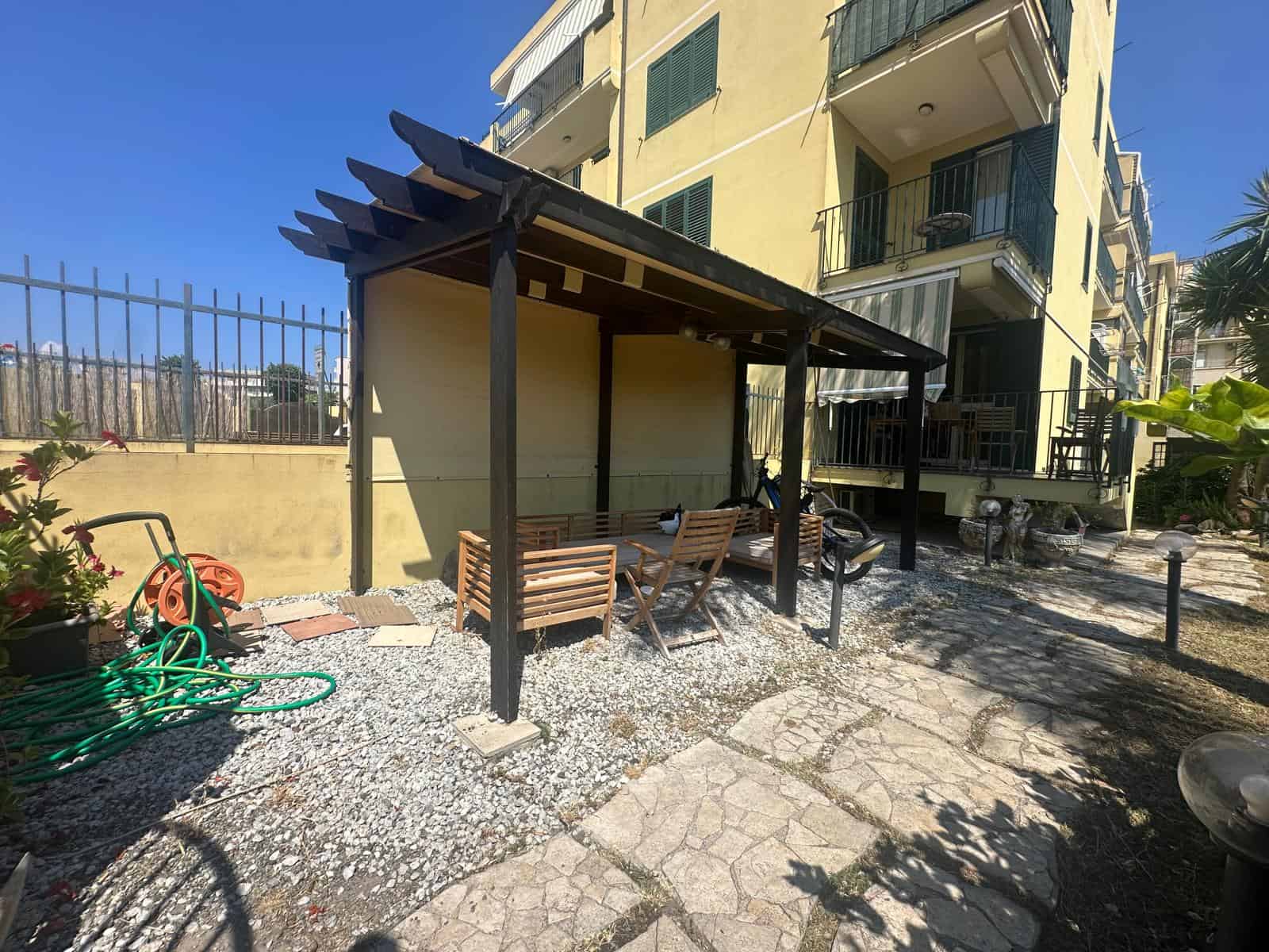 Spazio esterno con pergolato in legno, sedie e panchine, vicino a un edificio residenziale a Milazzo.