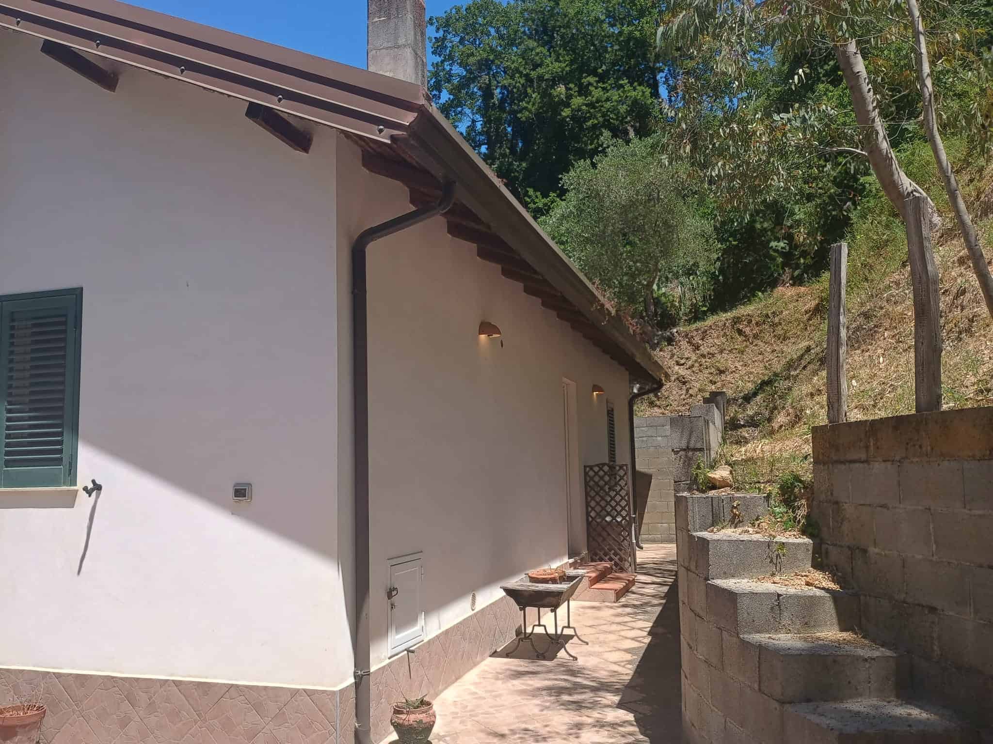 Ampio spazio esterno con scale in pietra, casa moderna con pareti bianche e finestre con persiane verdi, immersa nel verde e nella natura, ideale per vivere in tranquillità e comfort.