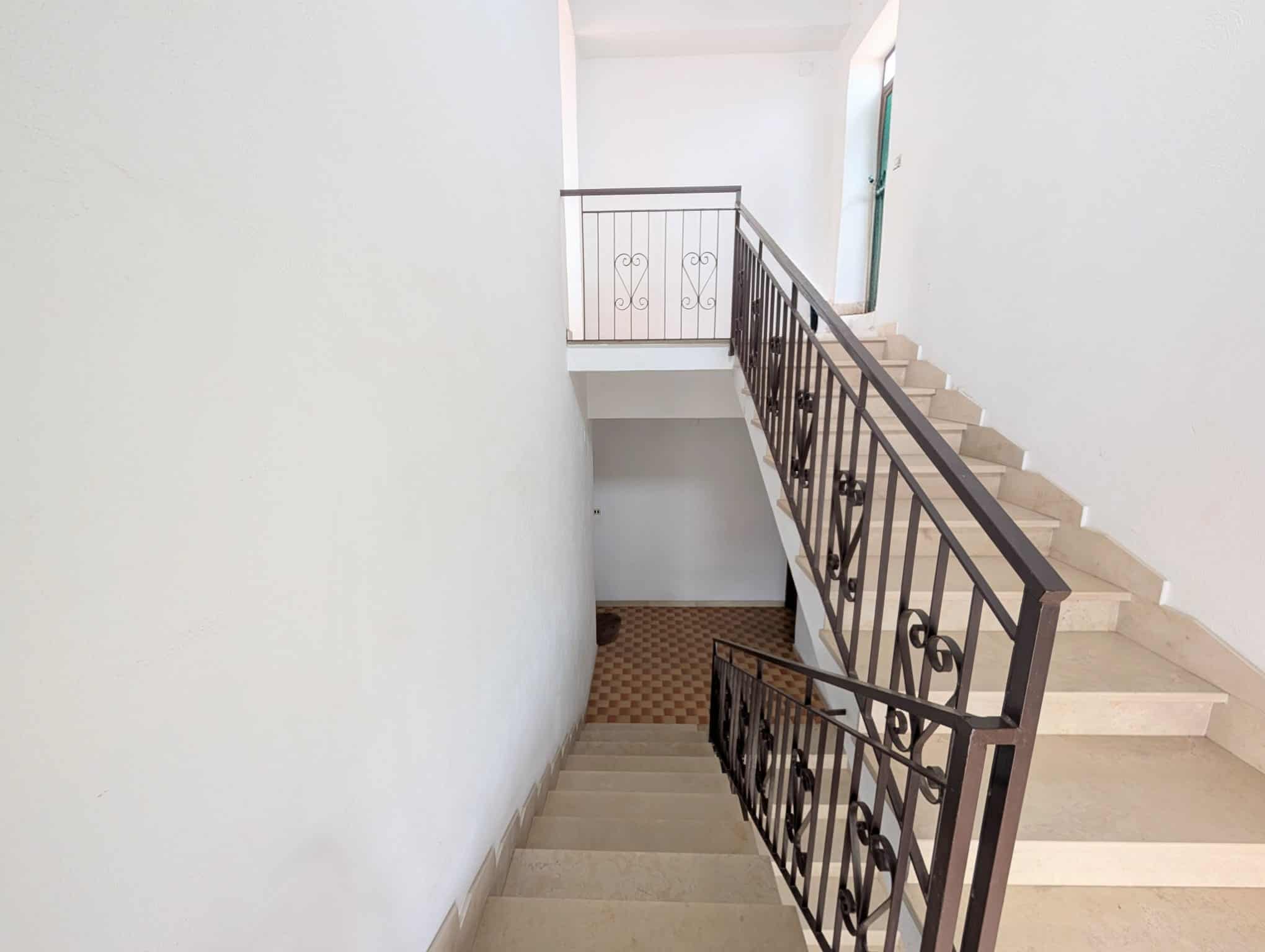 Scala interna di un edificio con ringhiera in ferro battuto e pareti bianche.