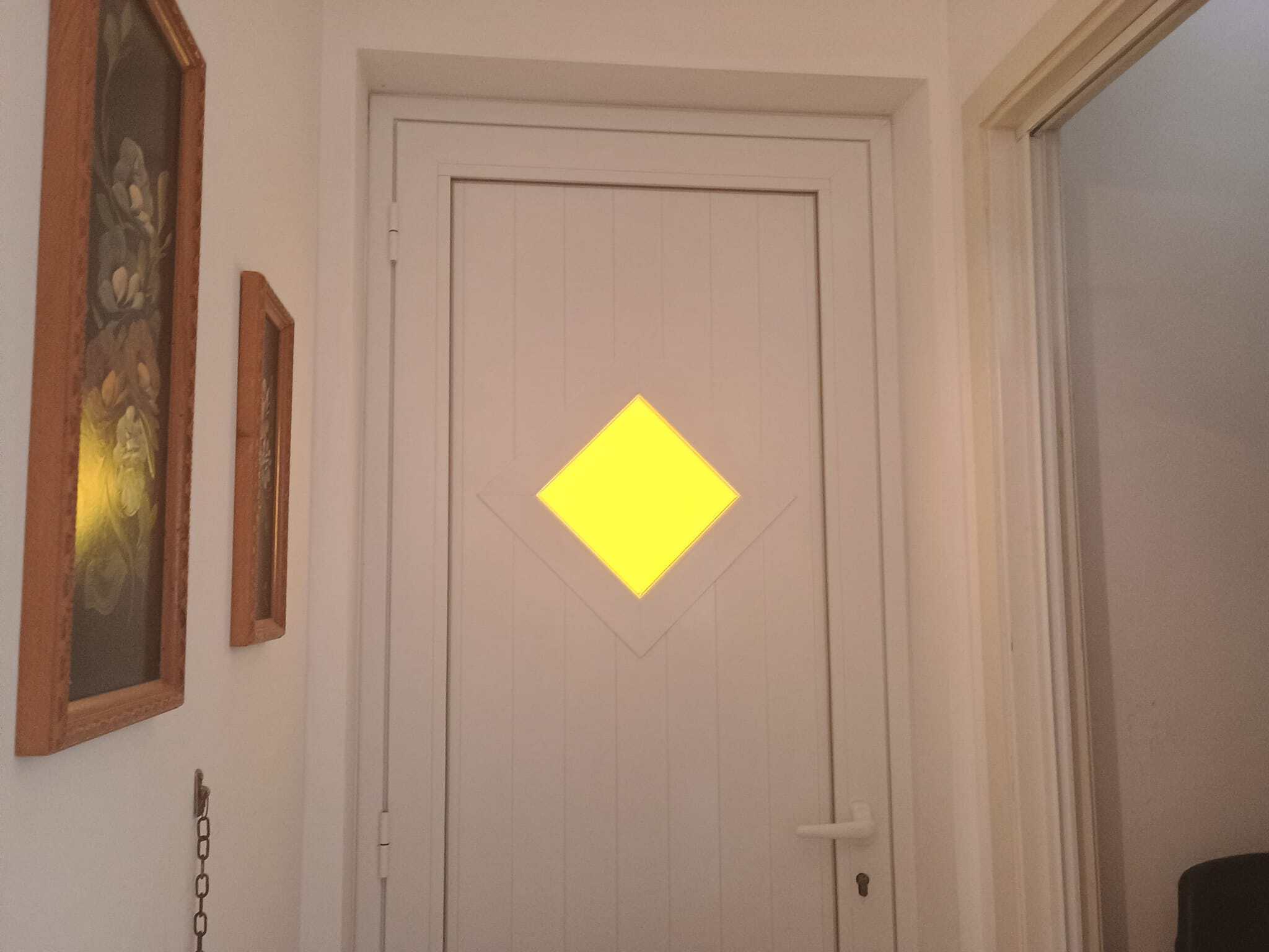 Porte bianca in stile moderno con decorazione a diamante gialla, situata in un ingresso domestico.