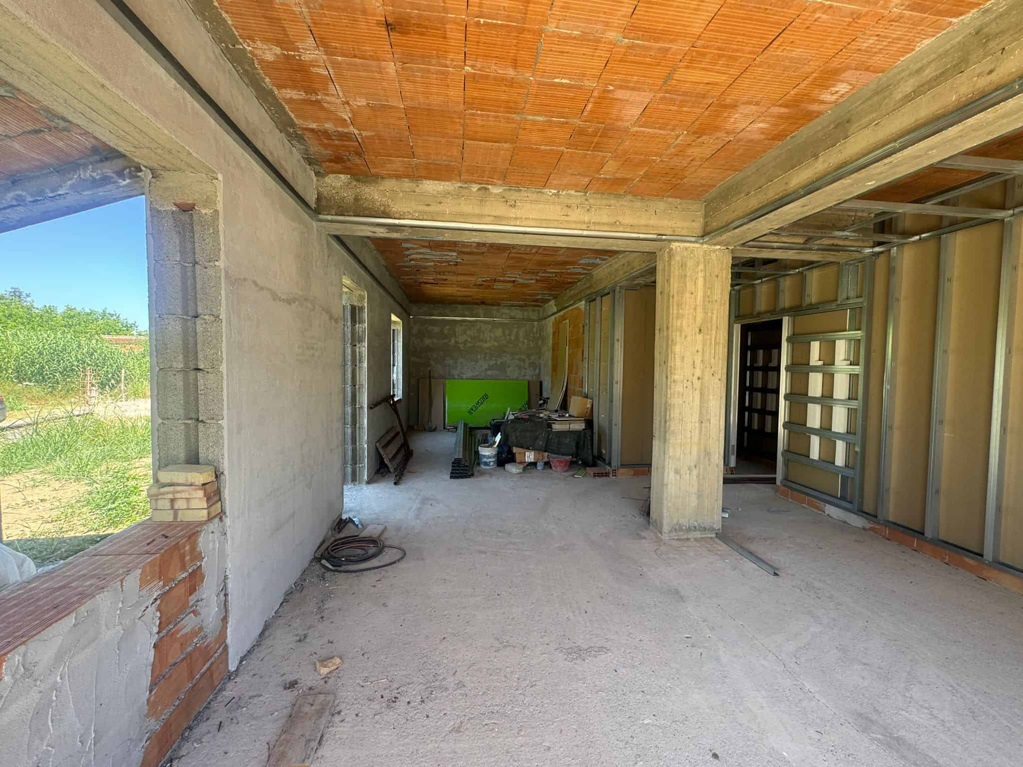 Interno di una casa in costruzione con pareti in cemento e soffitto in legno, spazio aperto con finestre e struttura in fase di completamento.
