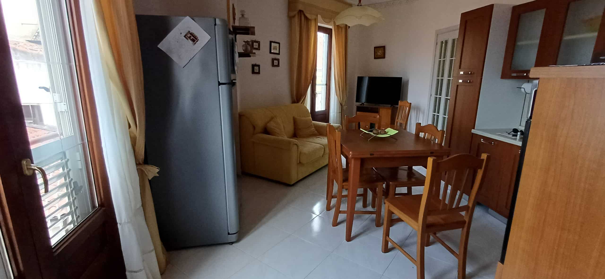 Interno di un appartamento NextCasa con soggiorno, cucina e zona pranzo, arredato in stile semplice e funzionale, con mobili in legno e elettrodomestici moderni.