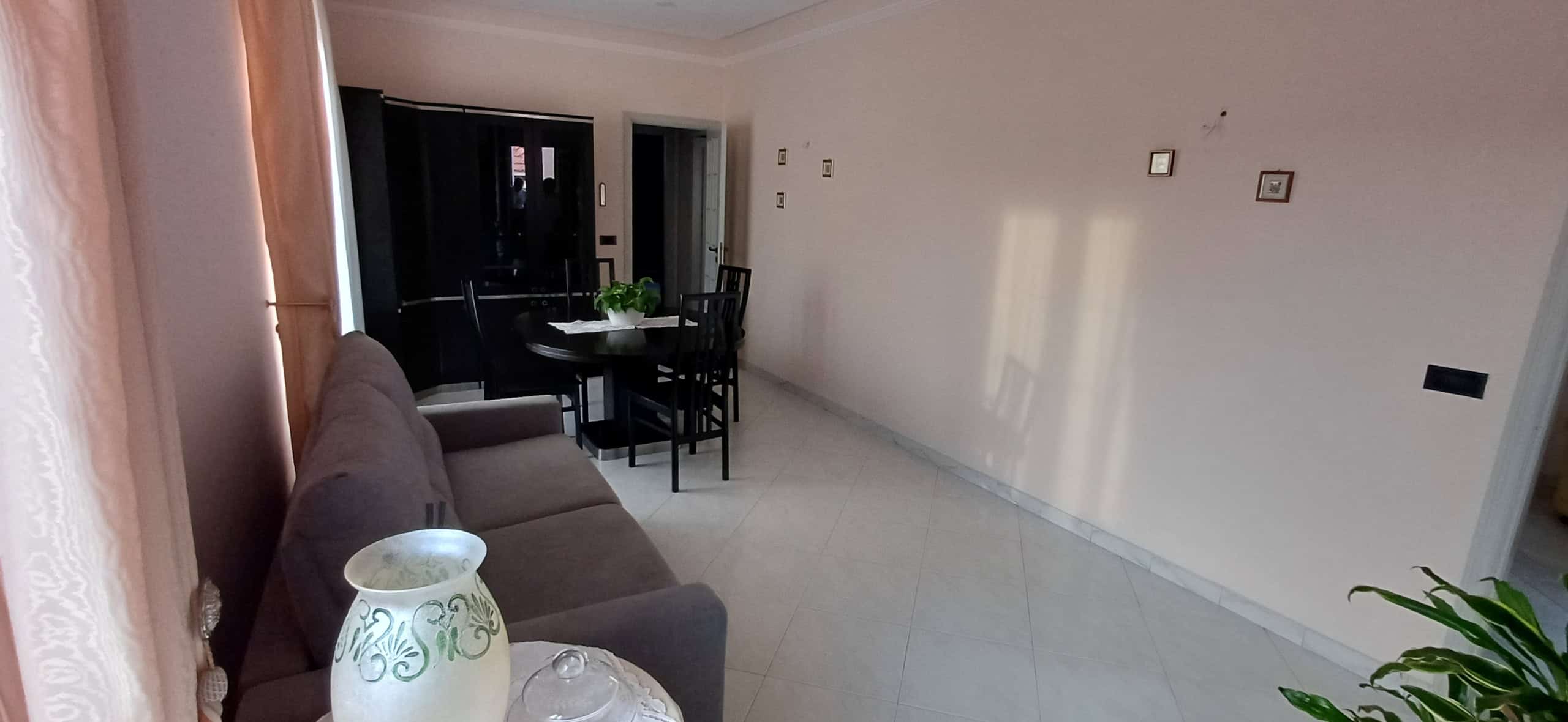 Interno di un soggiorno moderno con divano, tavolo da pranzo e piante, ambiente luminoso e accogliente.
