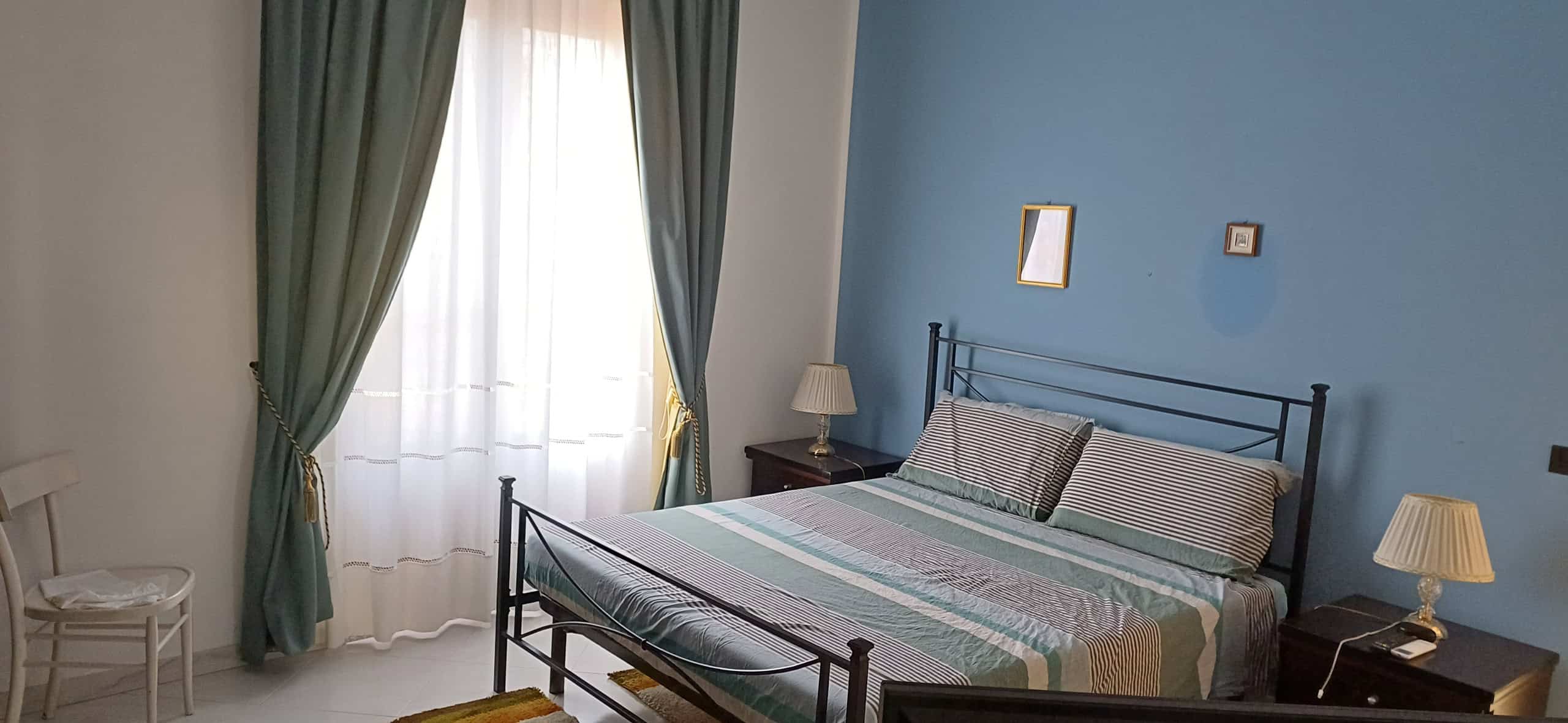 Camera da letto elegante con letto matrimoniale, tende verdi e lampade da comodino, ambiente luminoso e accogliente.