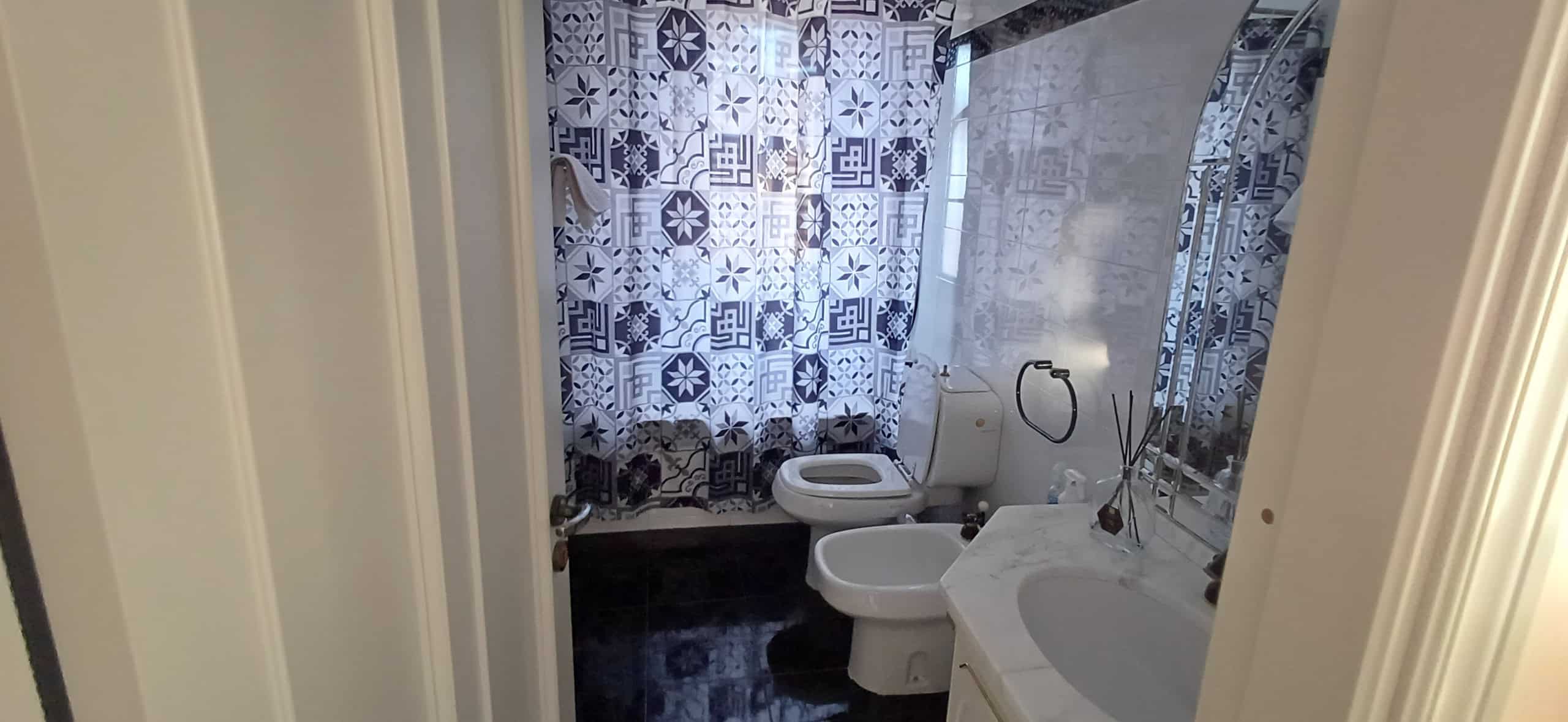 Bagno con sanitari bianchi, specchio grande e dettagli decorativi sulle pareti, illuminato da luce naturale e artificiale.