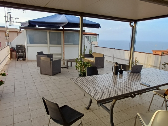 Terrazzo spazioso con tavolo, sedie e vista panoramica sul mare e sulla città, ideale per relax e socializzazione all'aperto.