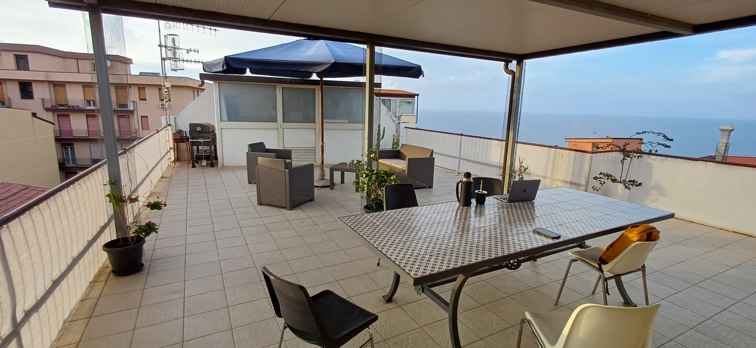 Terrazzo spazioso con tavolo, sedie e vista panoramica sul mare e sulla città, ideale per relax e socializzazione all'aperto.