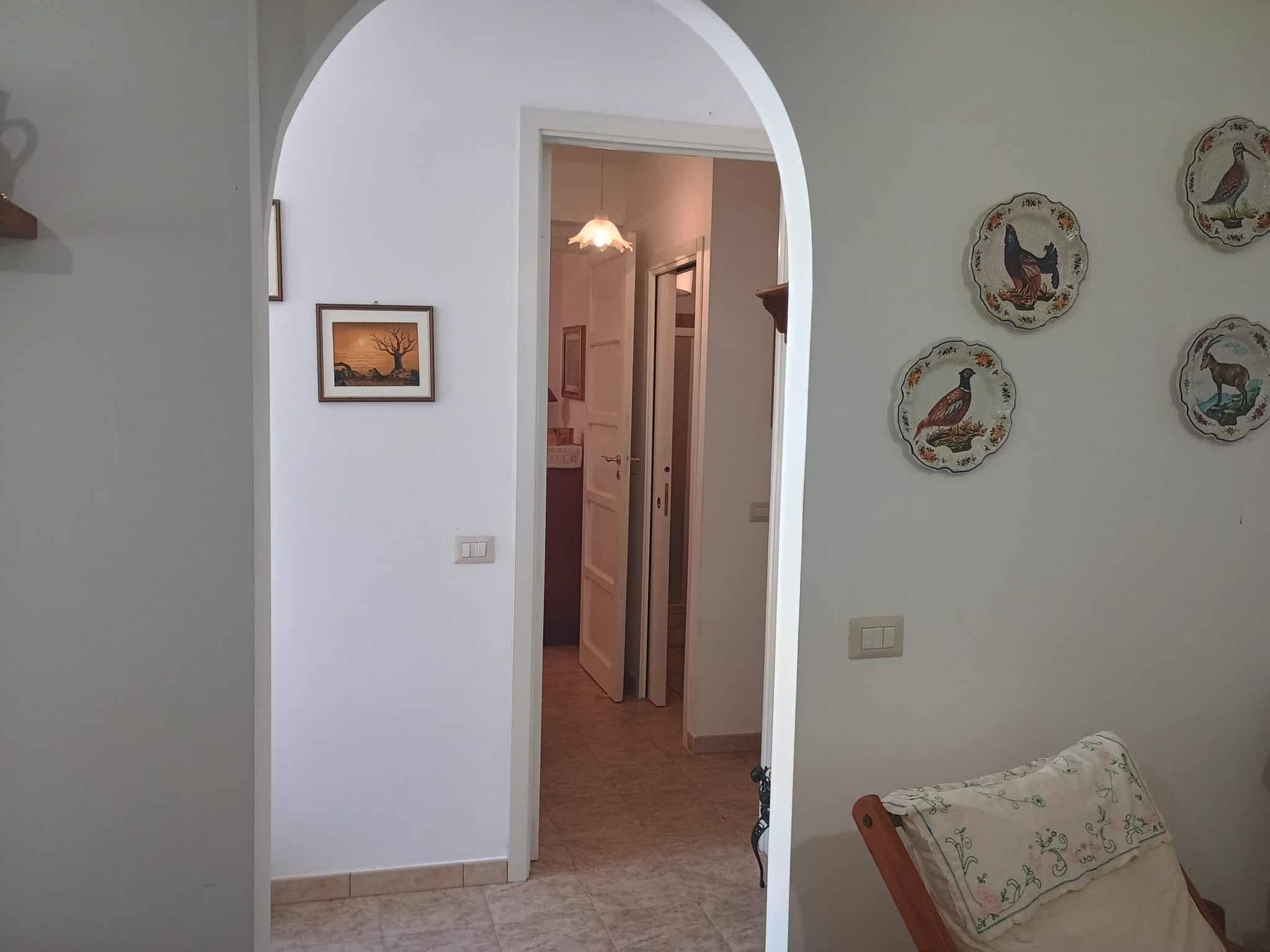 Interno di una casa con porta aperta, pareti bianche e decorazioni di piatti artistici, ambiente luminoso e accogliente, ideale per residenze di qualità a NextCasa.