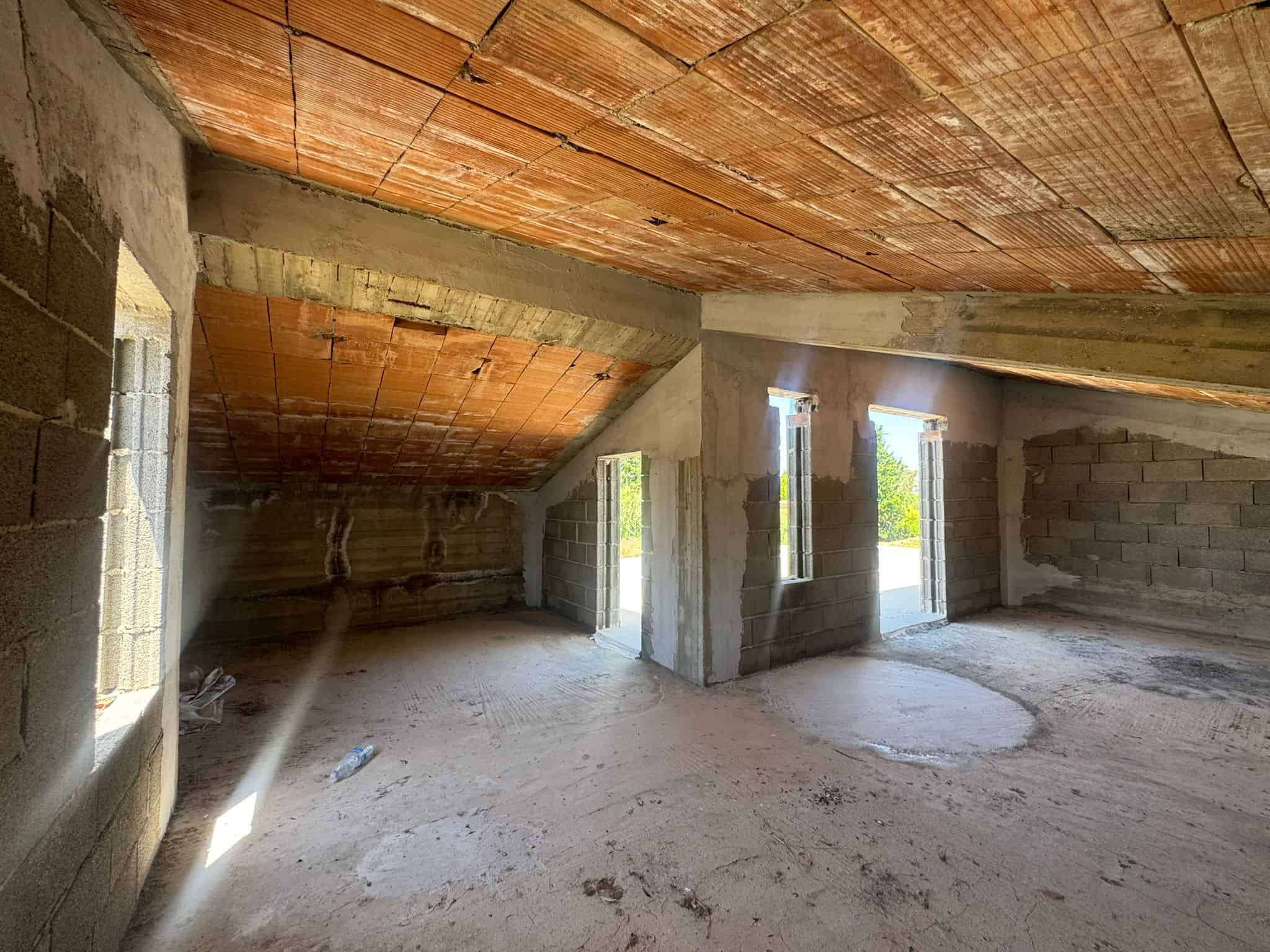 Interno di un edificio in costruzione con pareti in cemento e soffitto in legno, pronto per finiture.