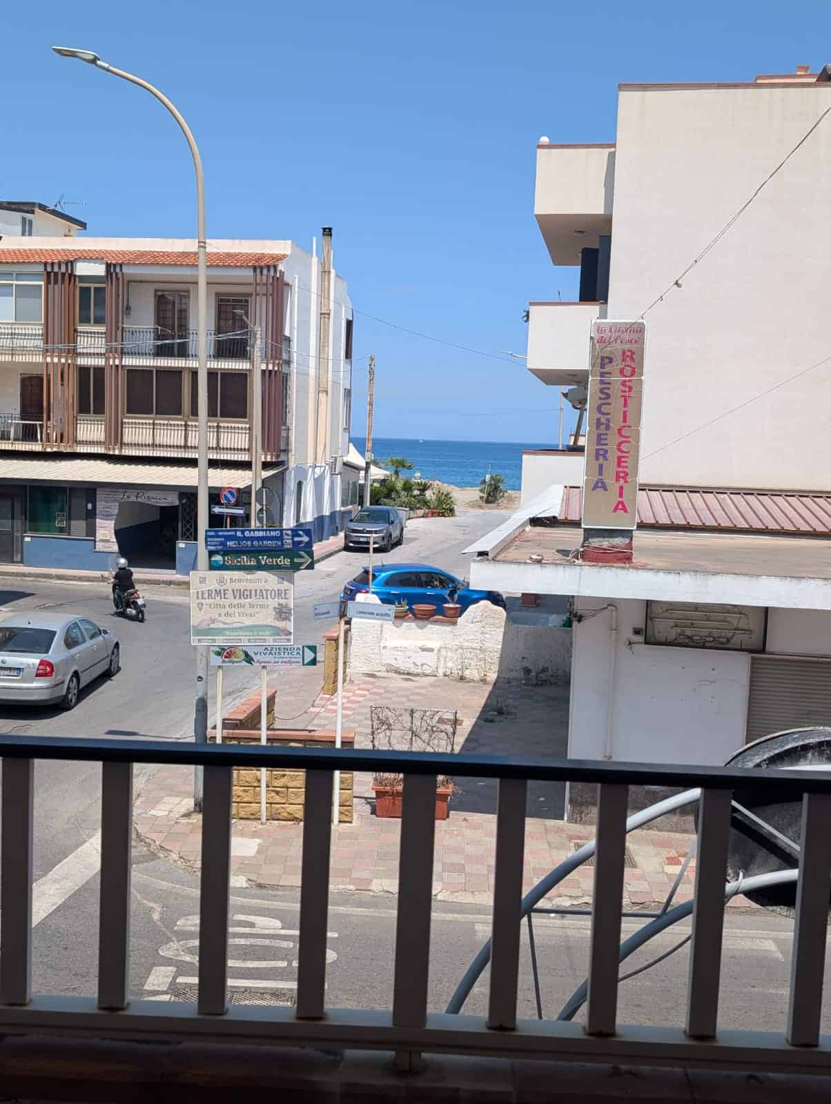 Vista mare dal balcone di un appartamento a NextCasa, con strada e edifici circostanti, in una giornata soleggiata.