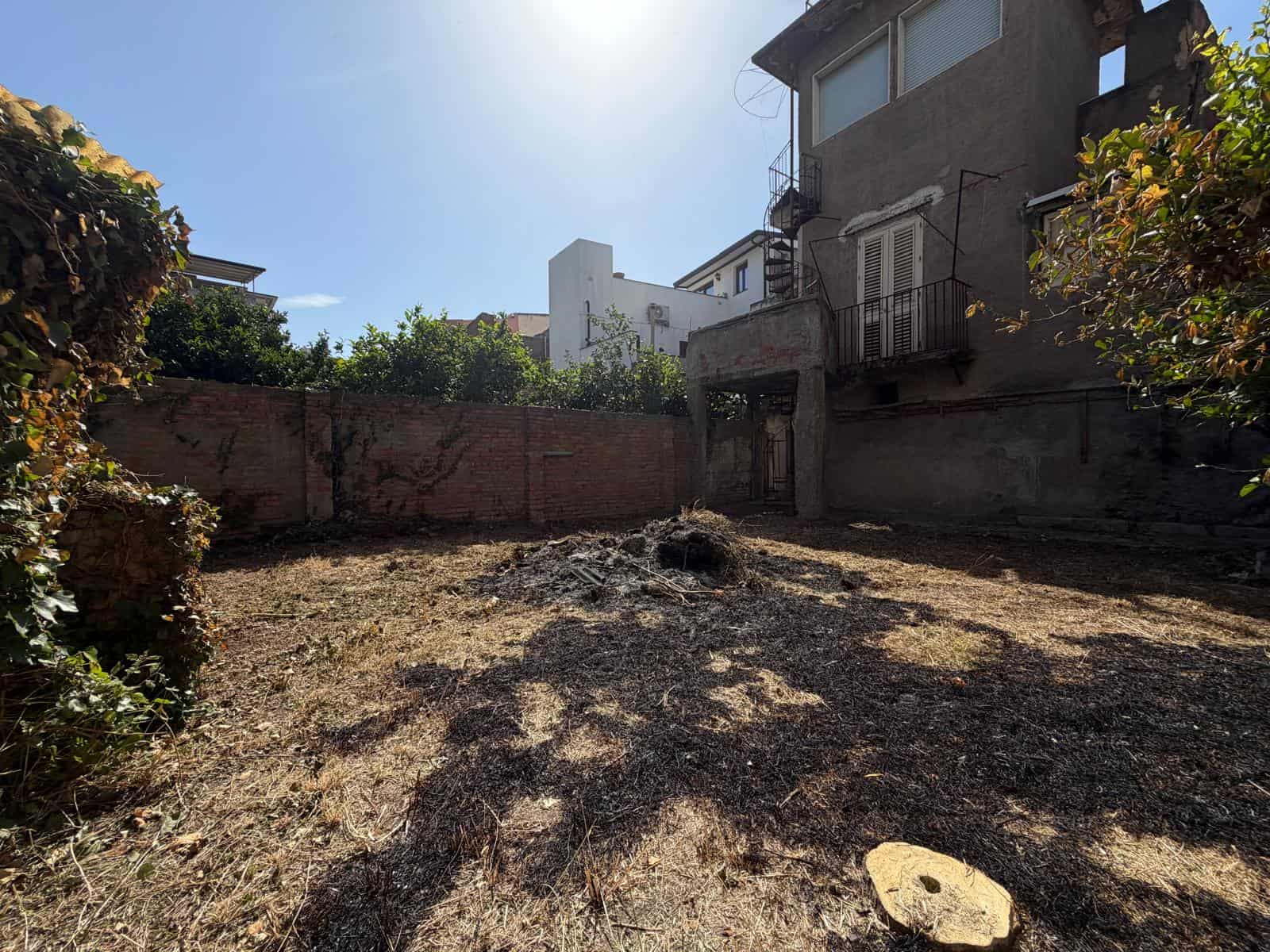 Spazio esterno di una casa indipendente in vendita a Barcellona P.G., con giardino recintato e edifici circostanti.
