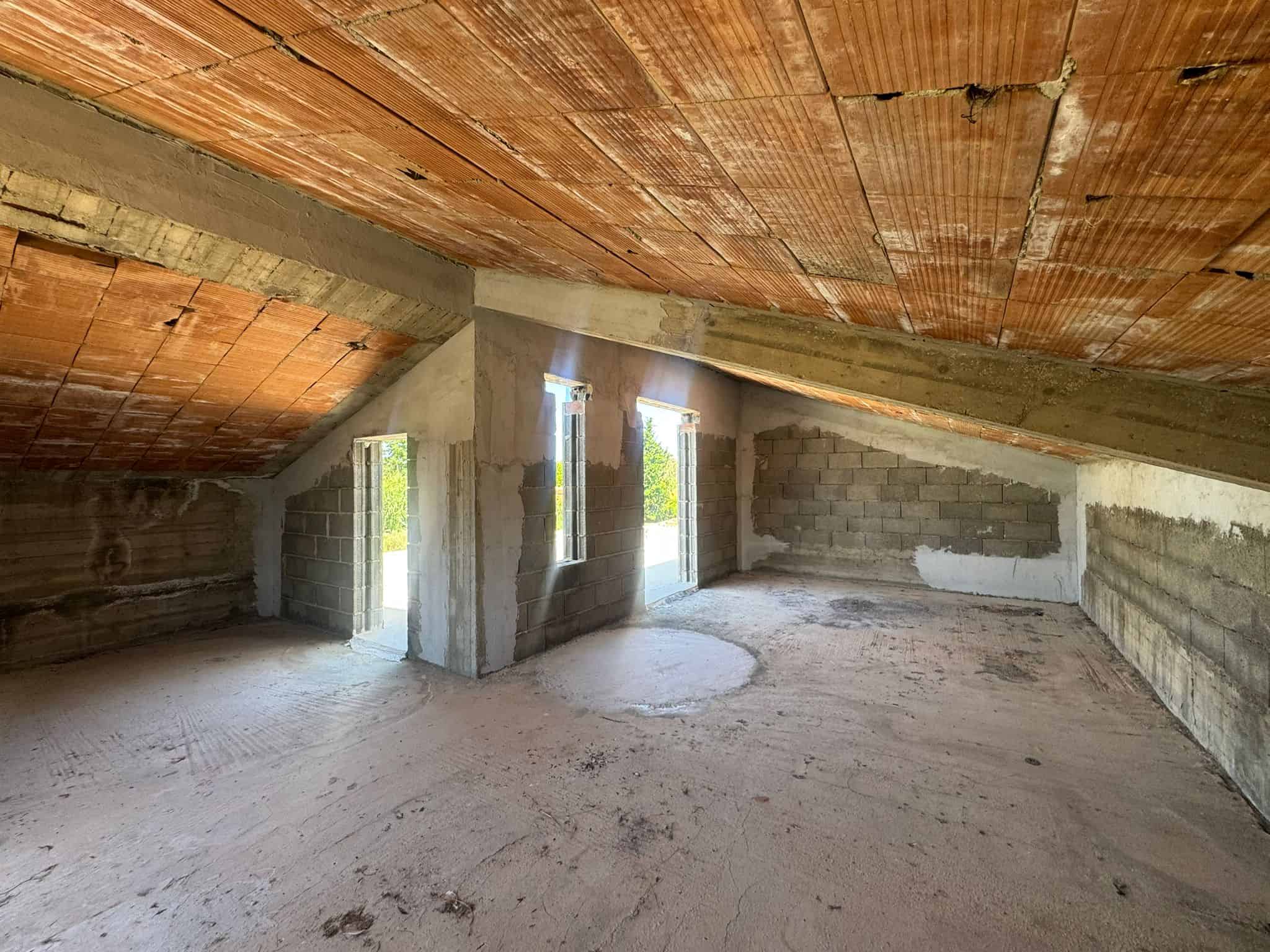 Interno di un attico in costruzione con pareti in cemento e soffitto in legno, pronto per finiture.