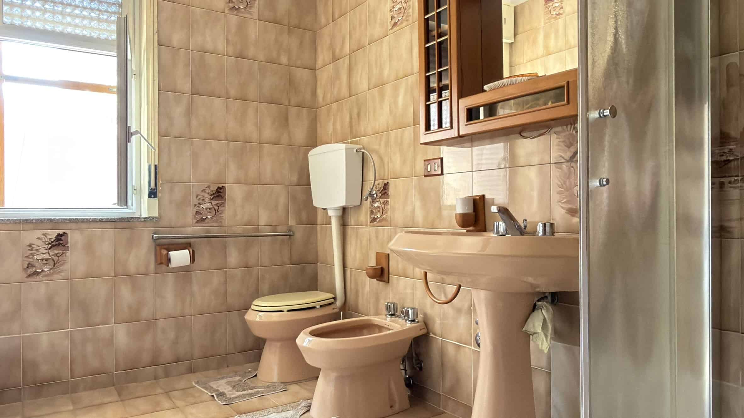 Bagno moderno con sanitari beige, lavabo e doccia in un ambiente luminoso e ben arredato.
