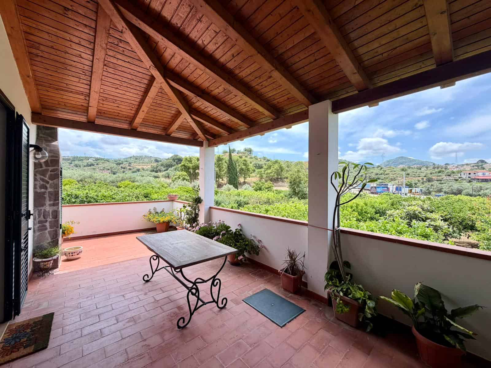Terrazza panoramica con vista su verde e colline, copertura in legno e arredi in stile rustico.