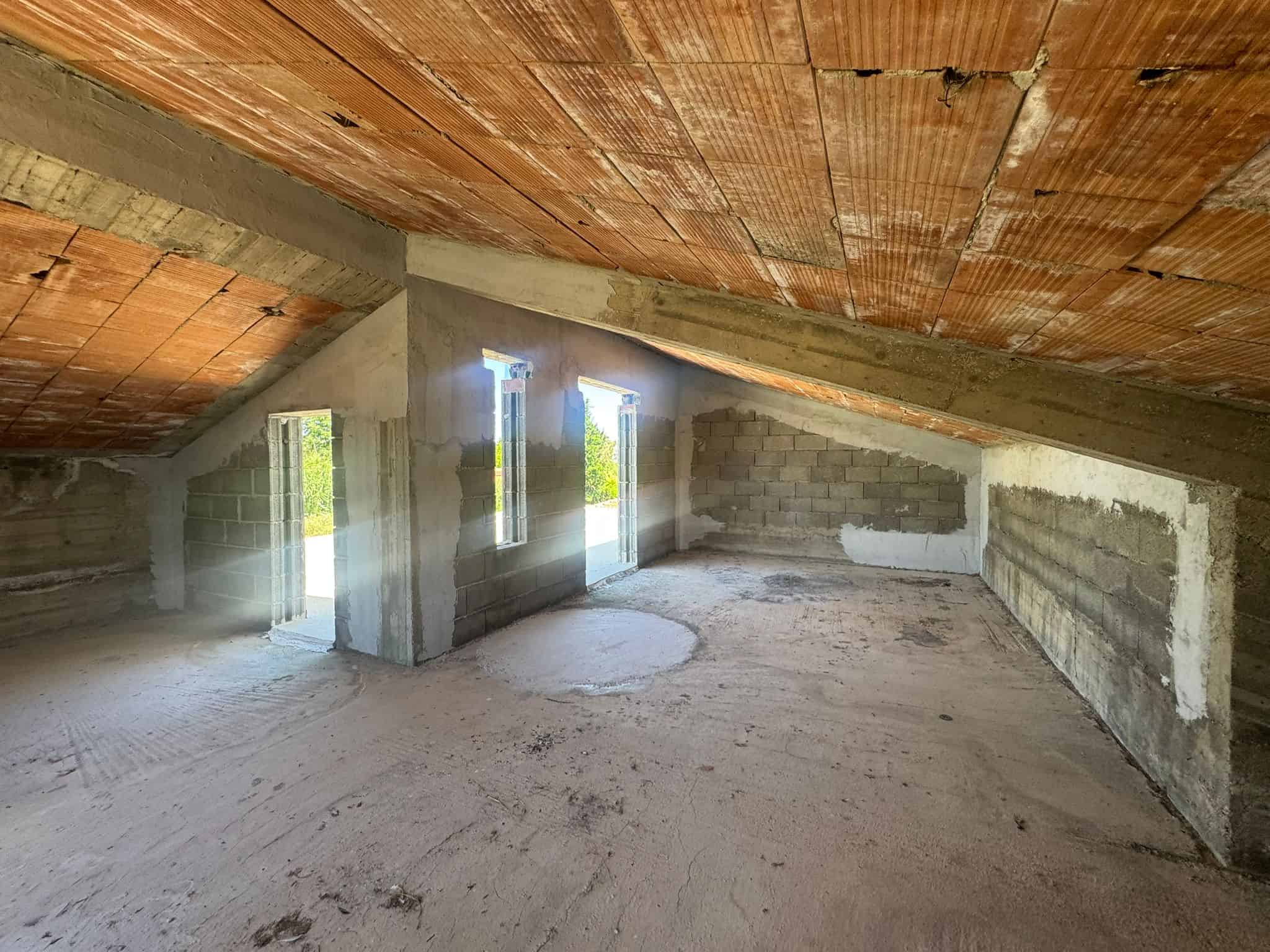Interno di un attico in costruzione con soffitto inclinato e pareti in cemento armato, pronto per finiture.